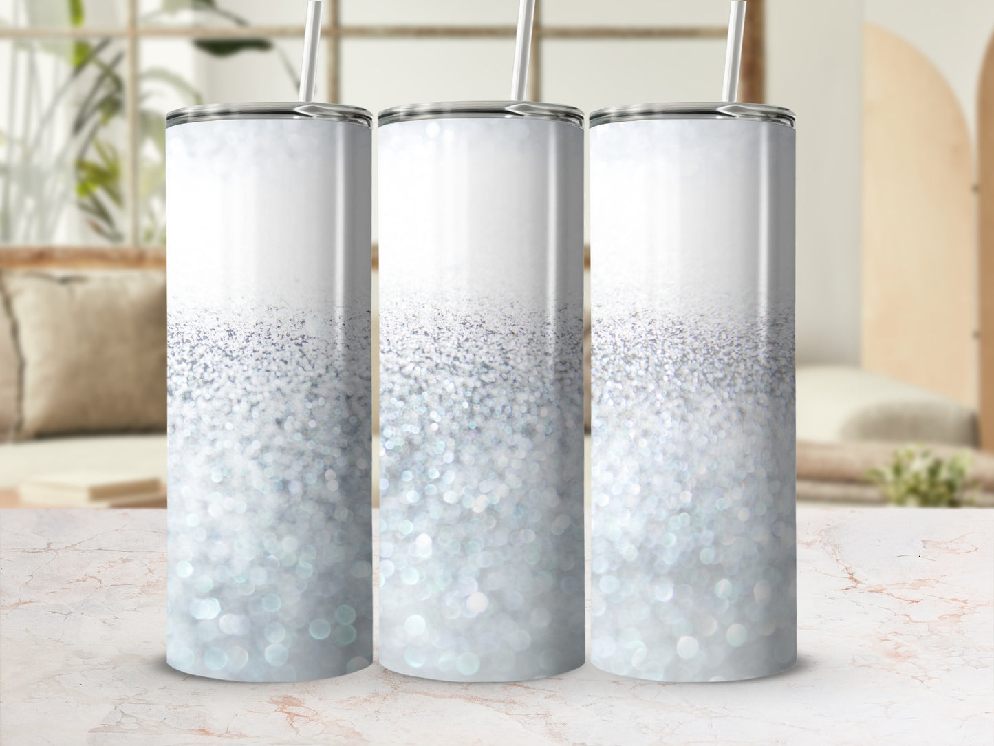 Three silver glitter tumblers with straws on a marble surface.