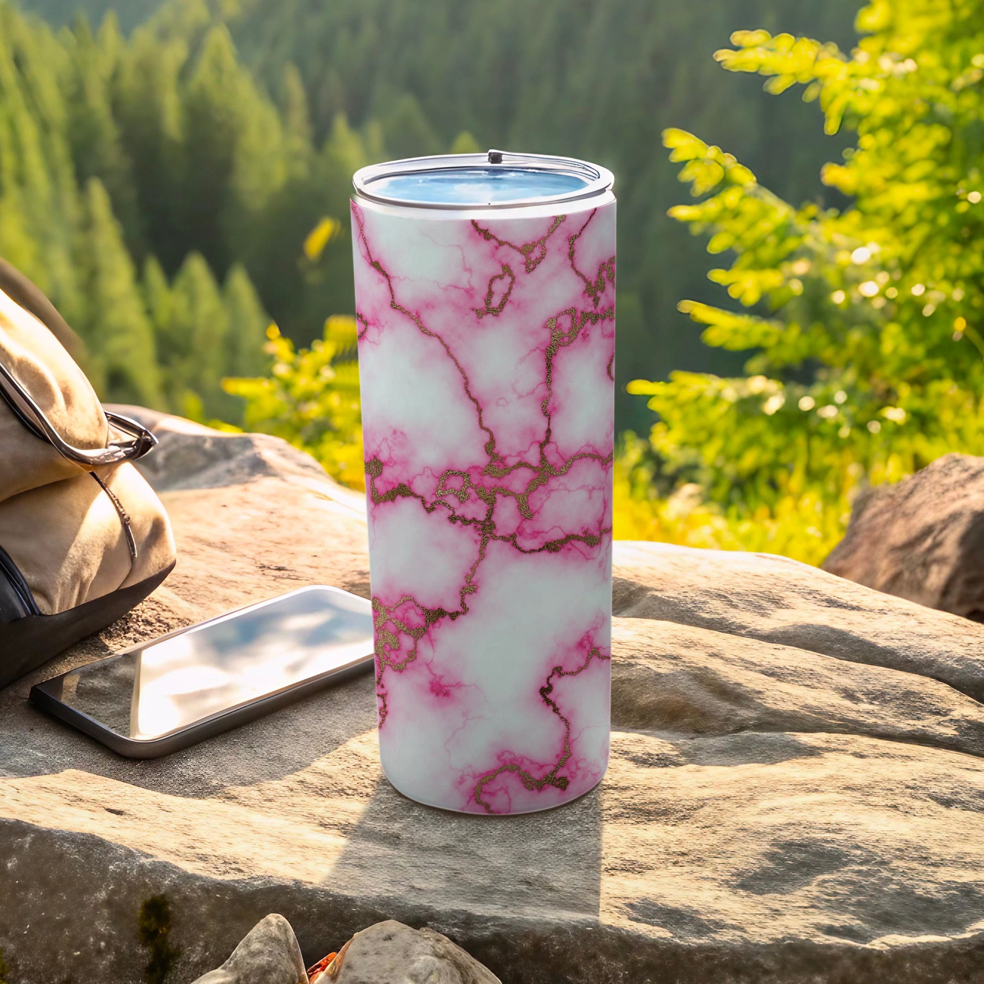 Pink and white marbled tumbler with gold accents on outdoor rock surface.