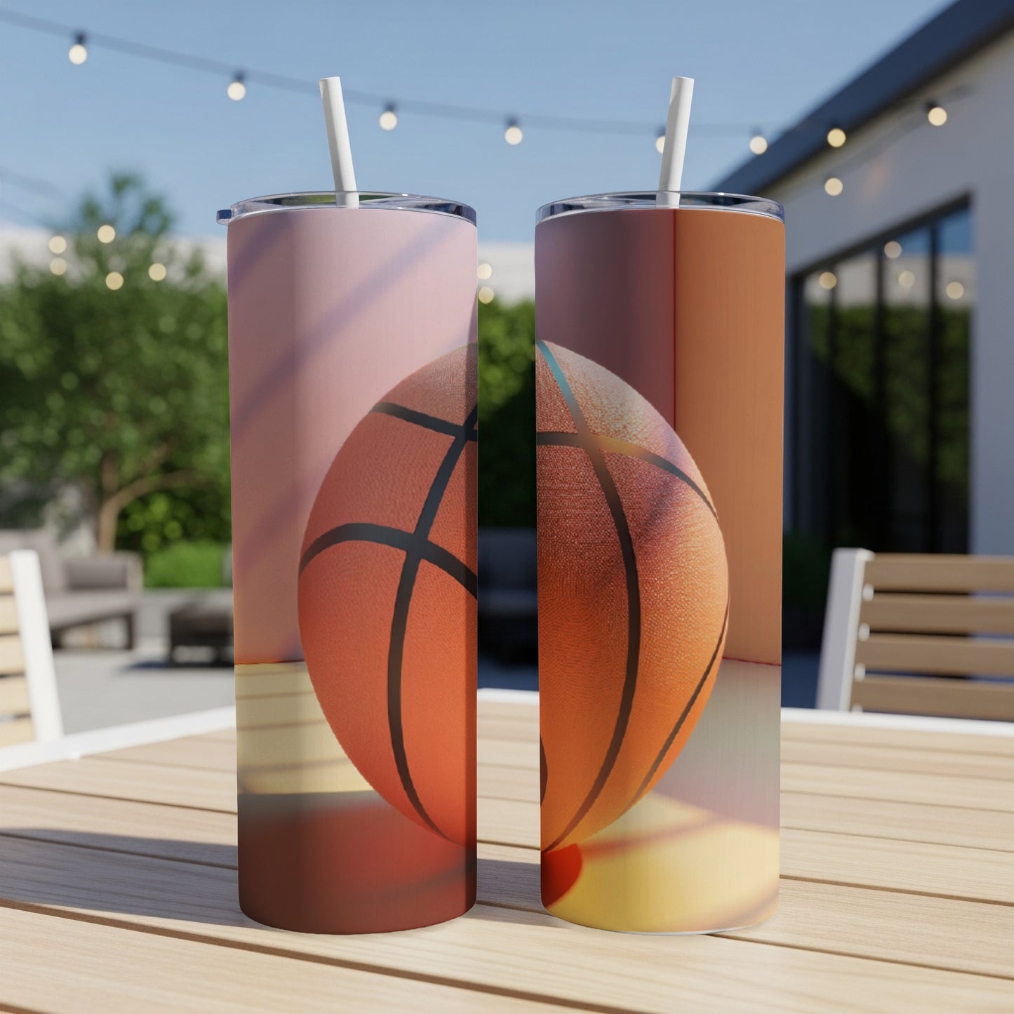Two basketball-themed tumblers with straws on a wooden table outdoors.