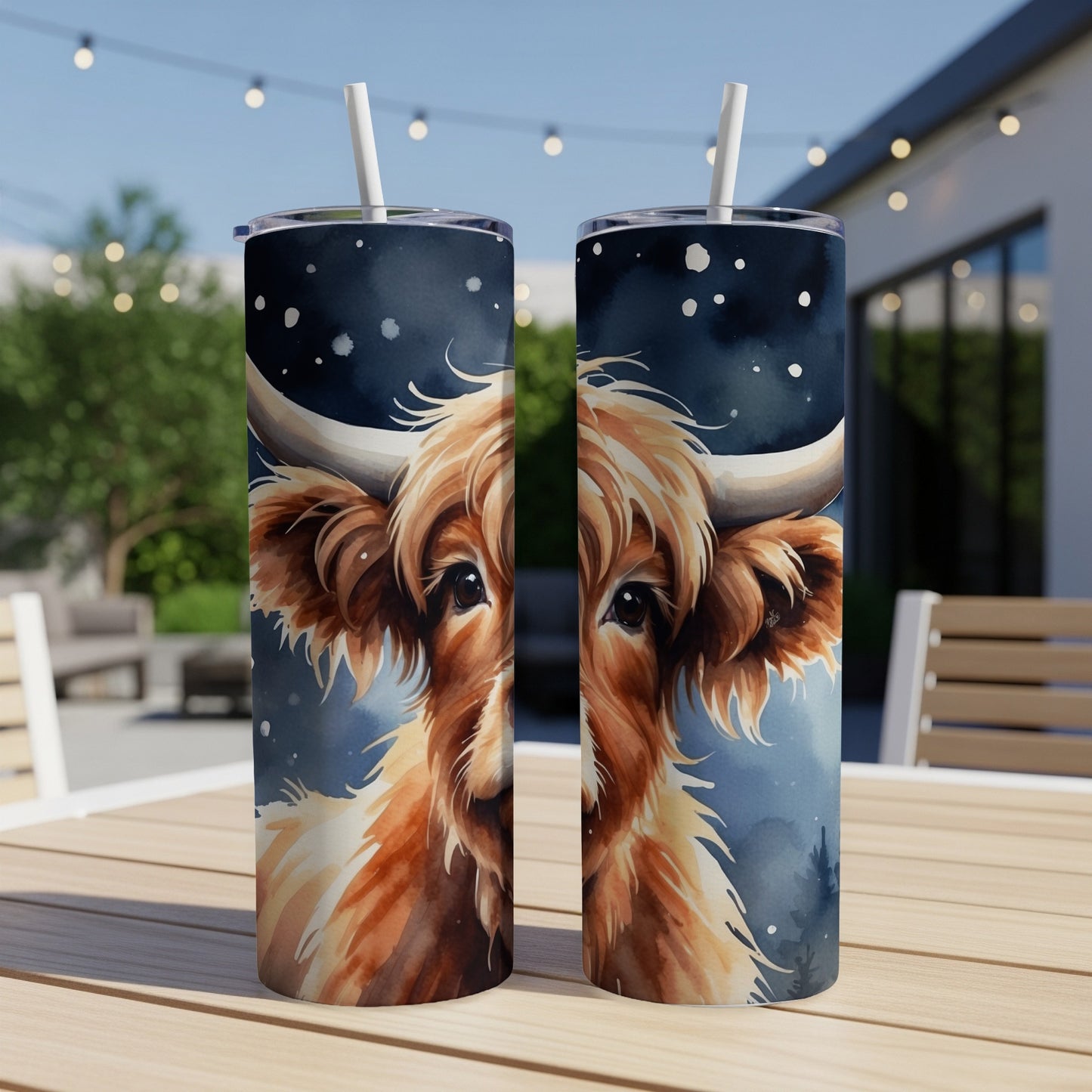 Two tumblers with a watercolor highland cow face design sit on a table.