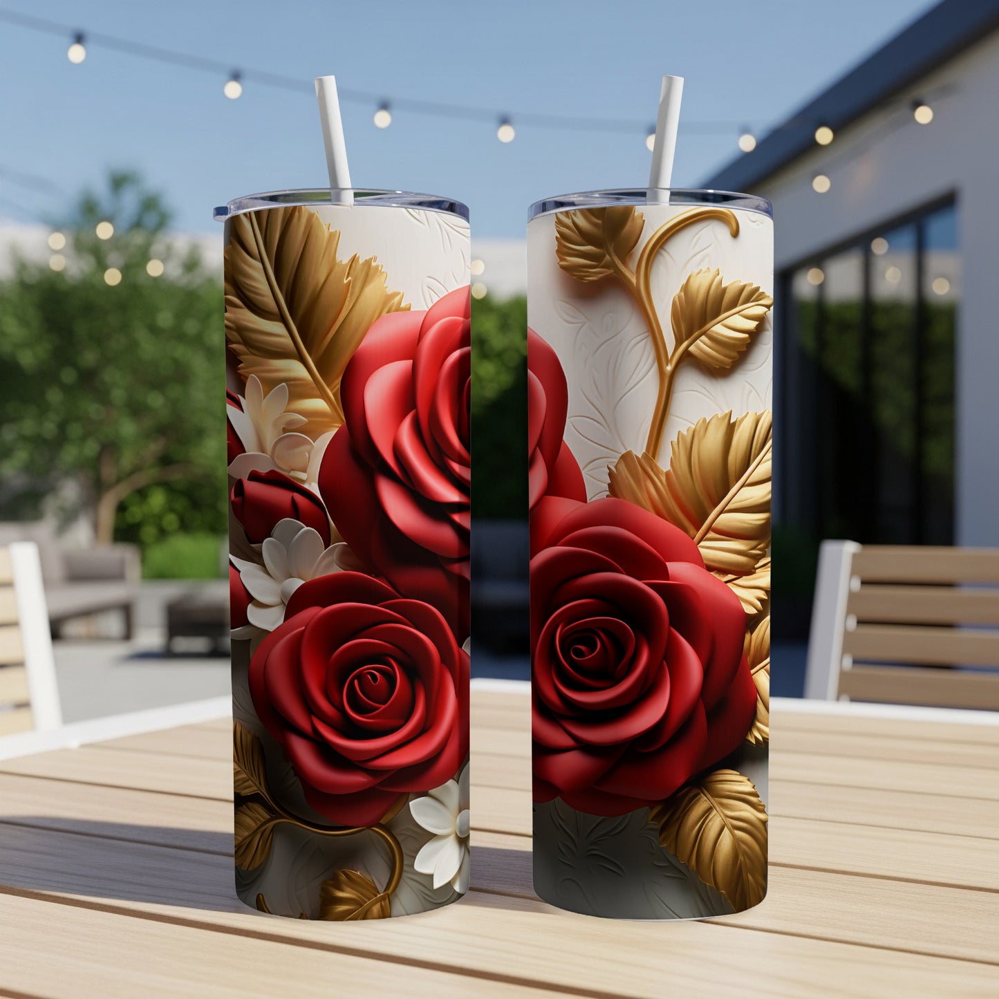 Two tall tumblers with red roses and gold leaves, set on a wooden table outdoors.