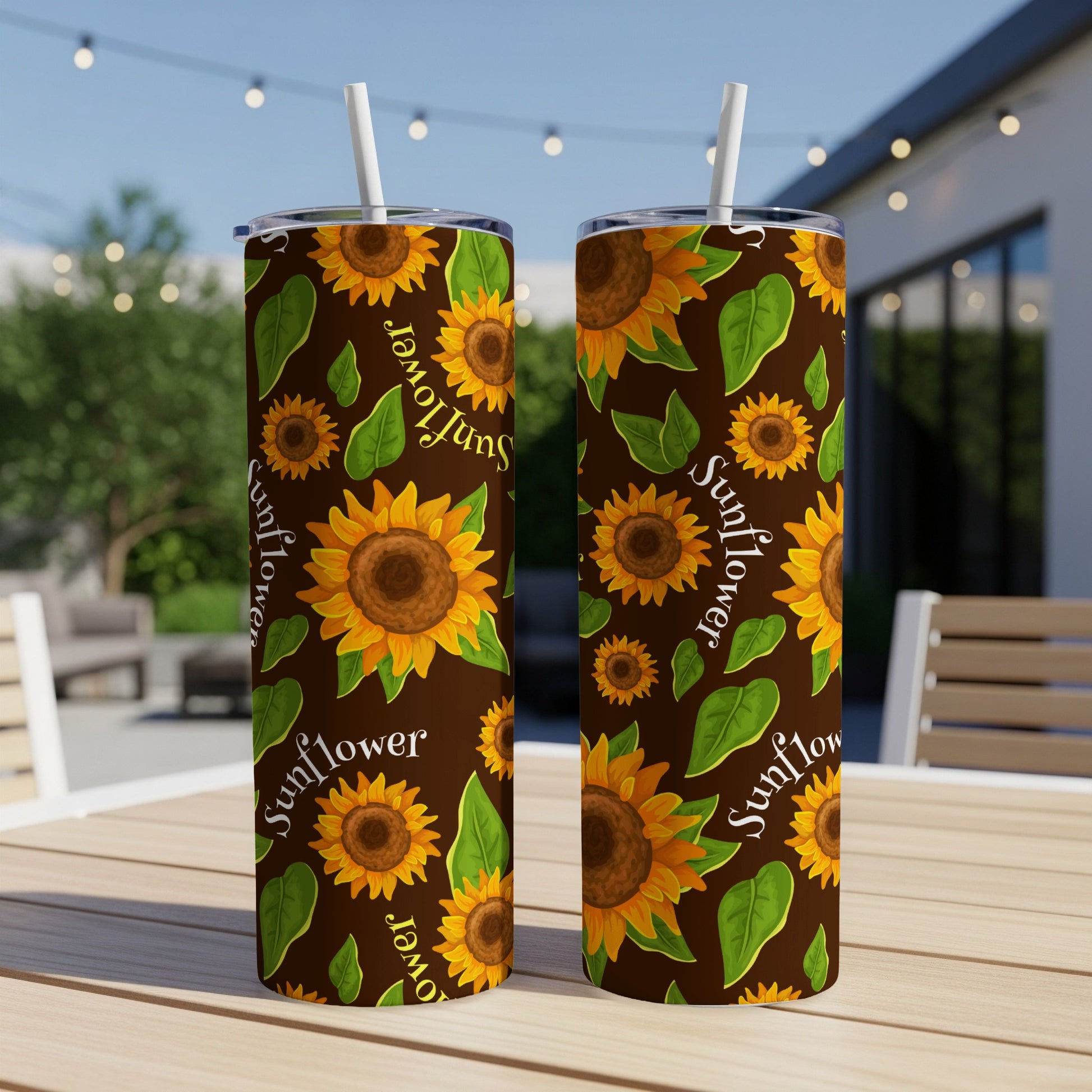 Two tumblers with sunflower pattern and straws, placed on a wooden table outdoors.