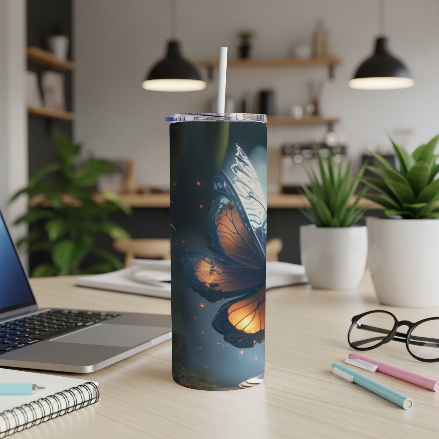 Tumbler with orange butterfly design, straw in top, on a desk.