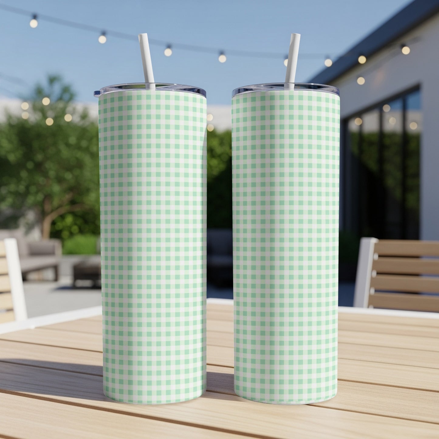 Two mint green and white checkered tumblers with straws on a wooden table.