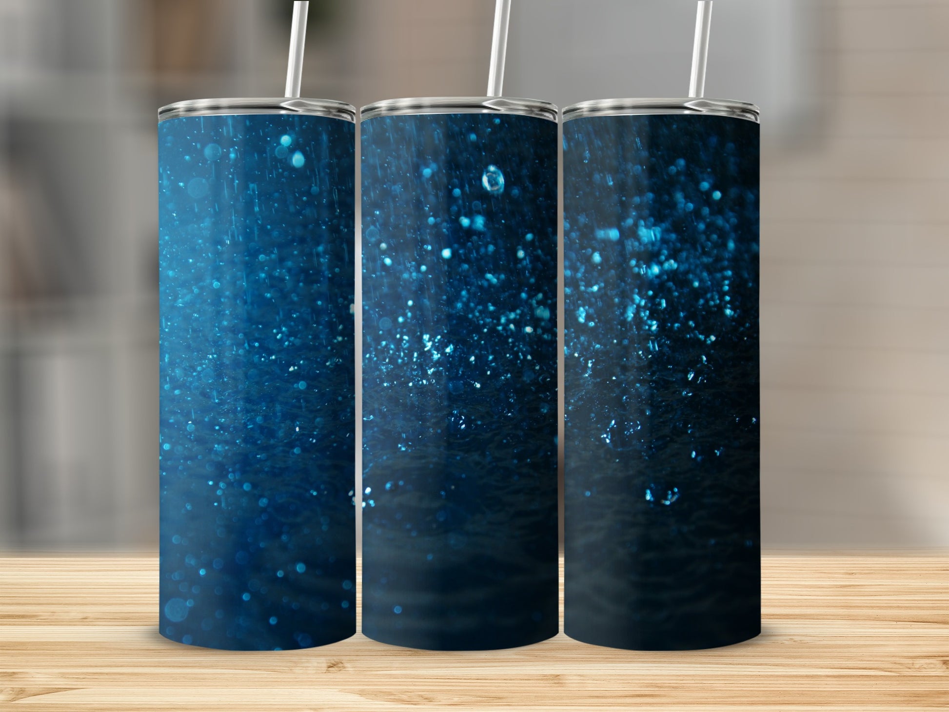 Three blue glitter tumblers with straws on a wooden surface.