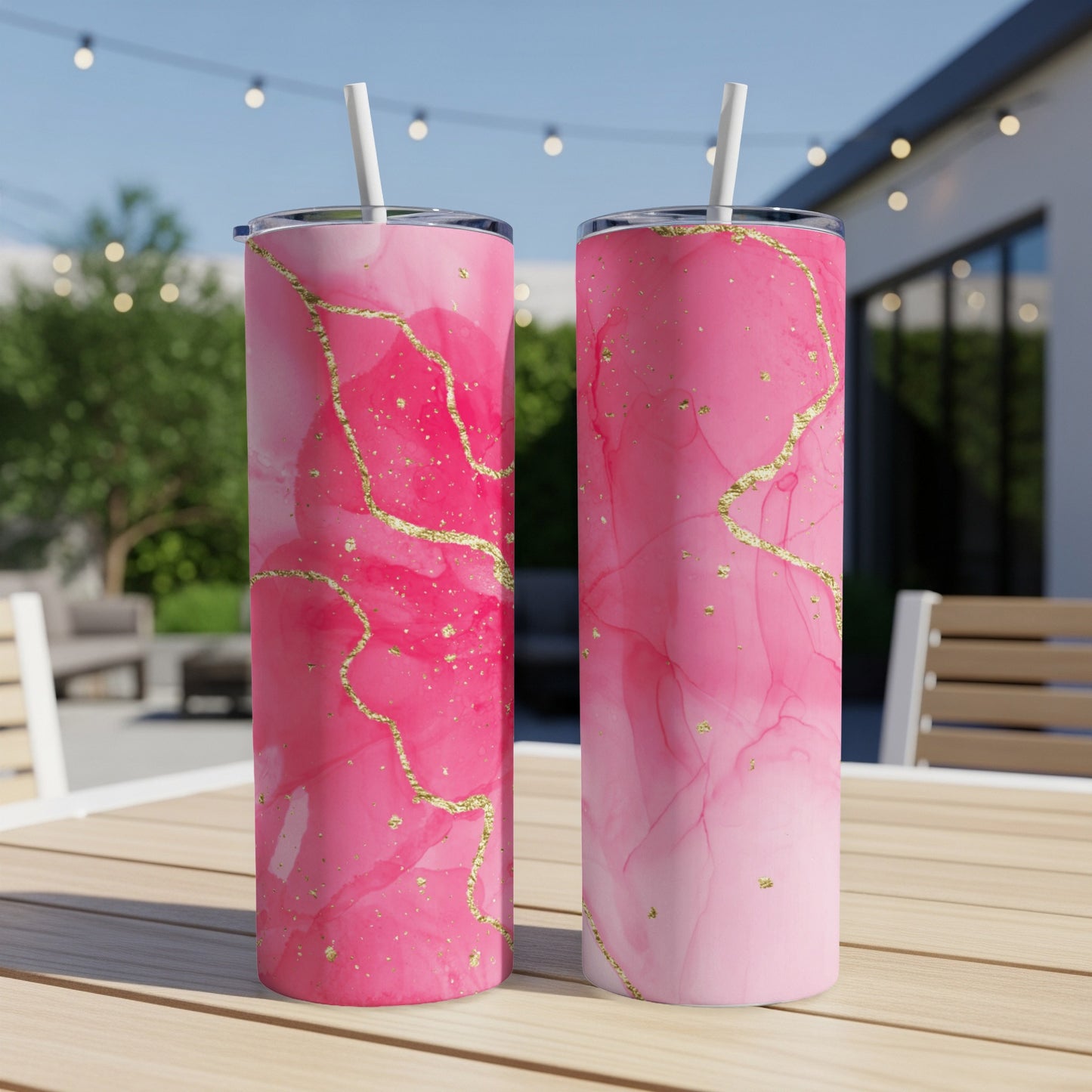 Two pink marble tumblers with gold accents on a table outdoors.
