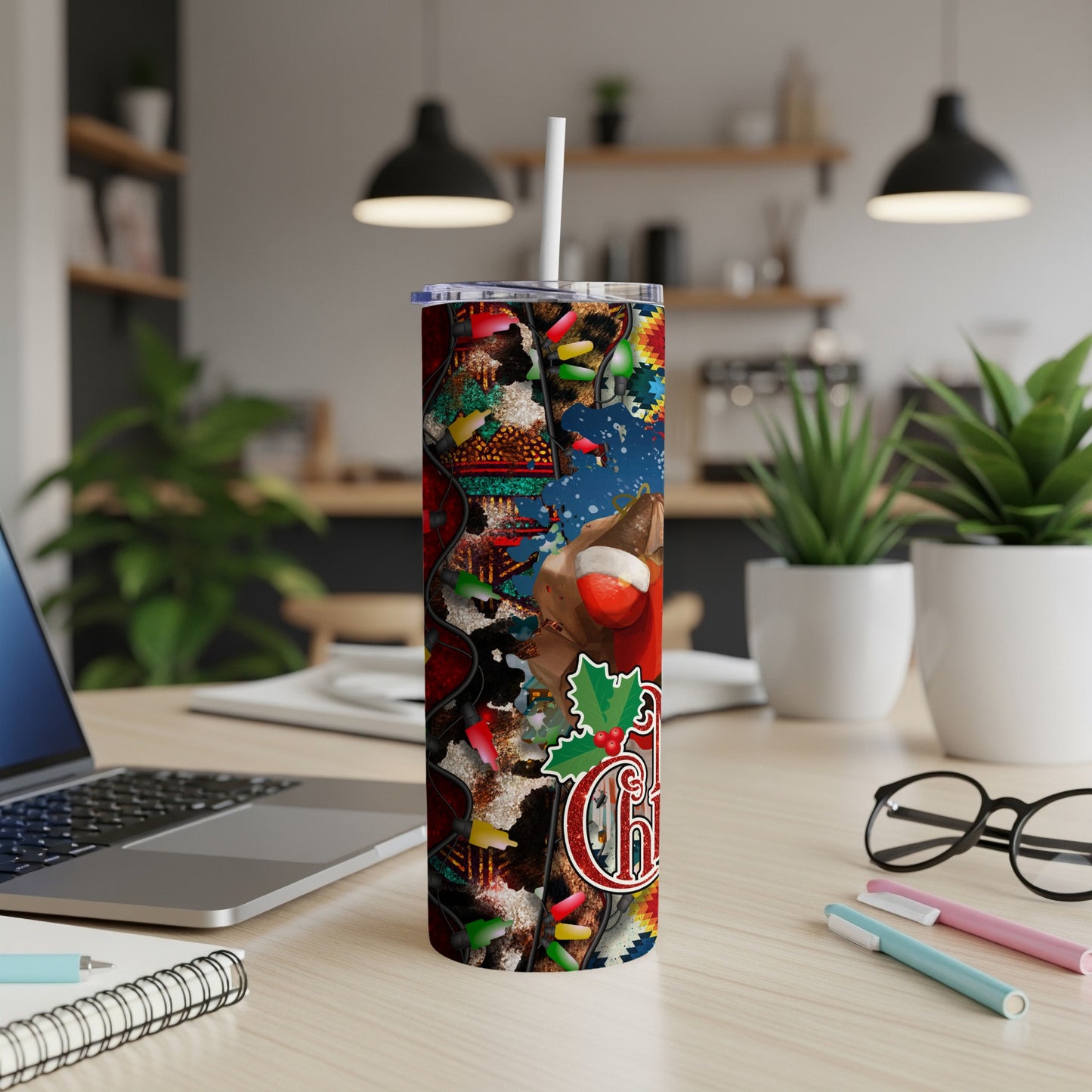 Tall tumbler with Christmas pattern, a mug, and laptop on a desk.