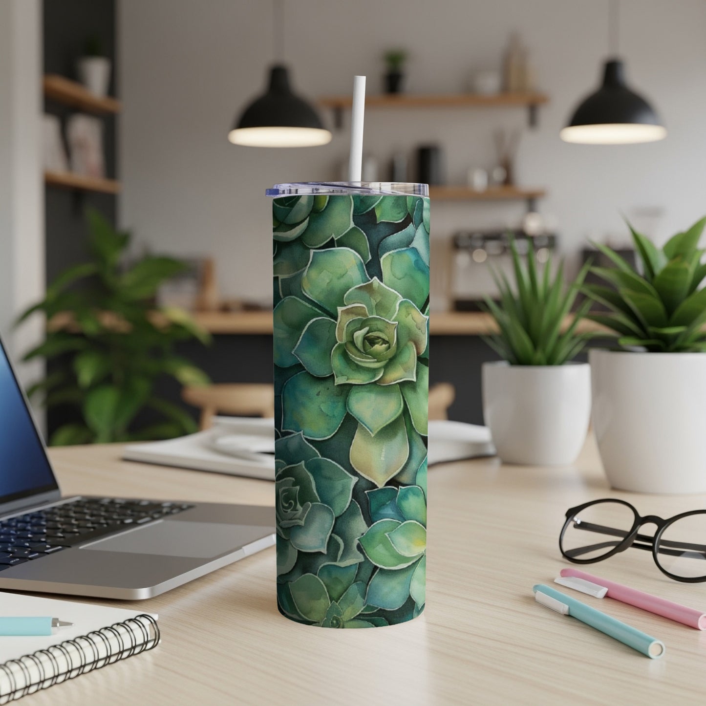 Tumbler with watercolor succulent pattern on desk with laptop and pens.
