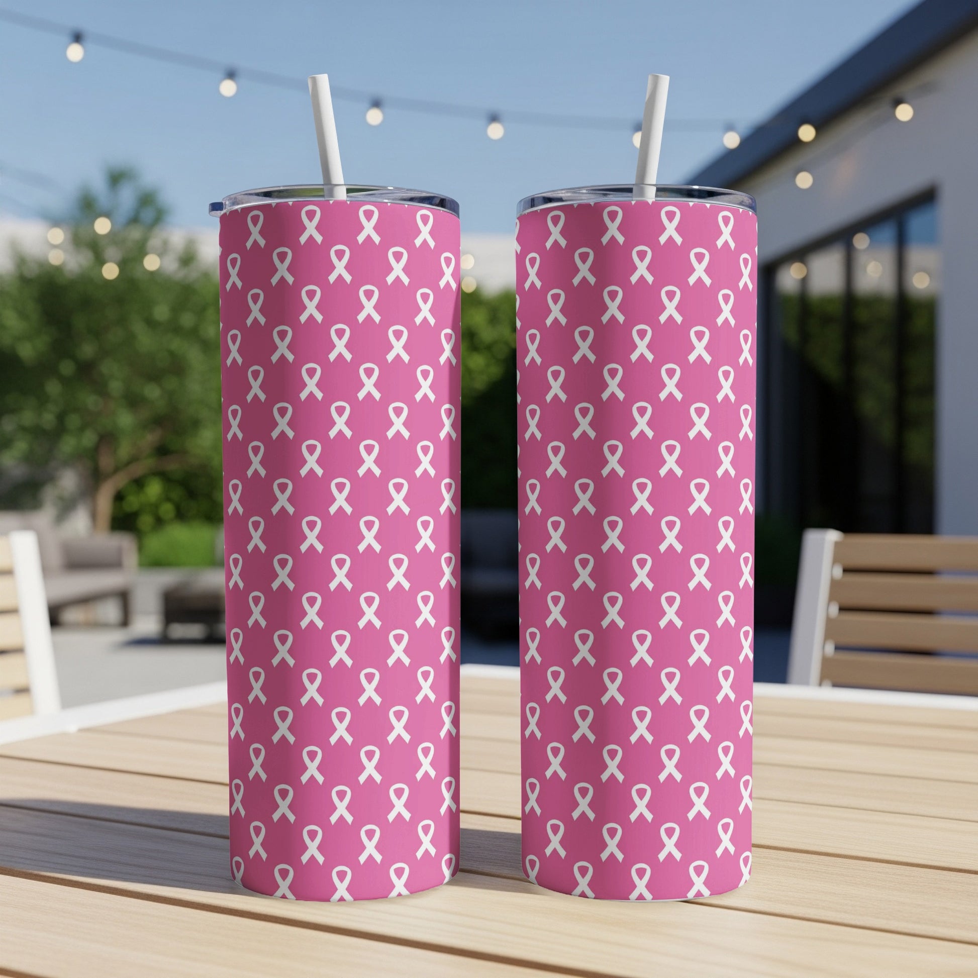 Two pink tumblers with white ribbon pattern and straws, displayed outdoors.