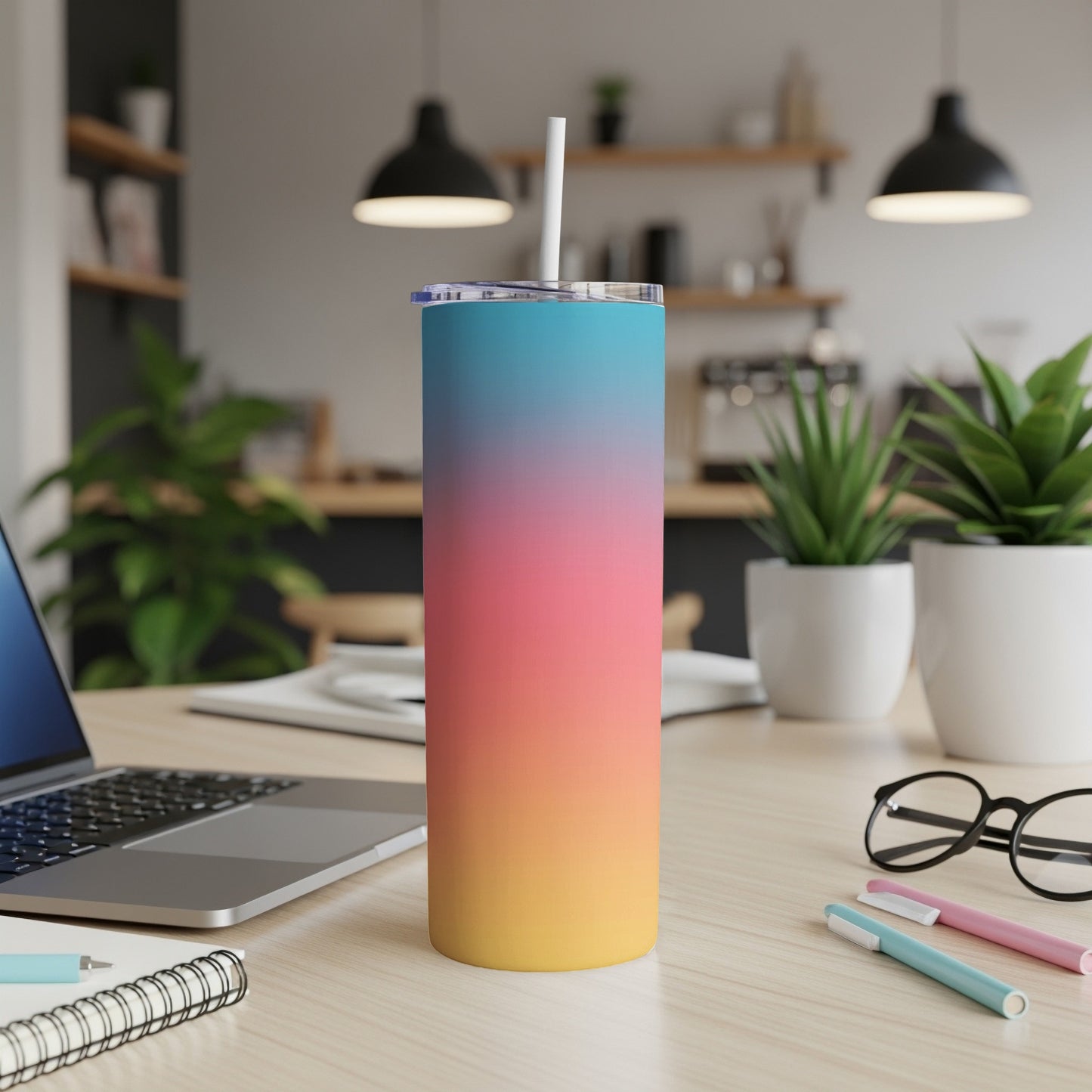 Gradient pink, orange, and blue insulated tumbler with straw on desk.