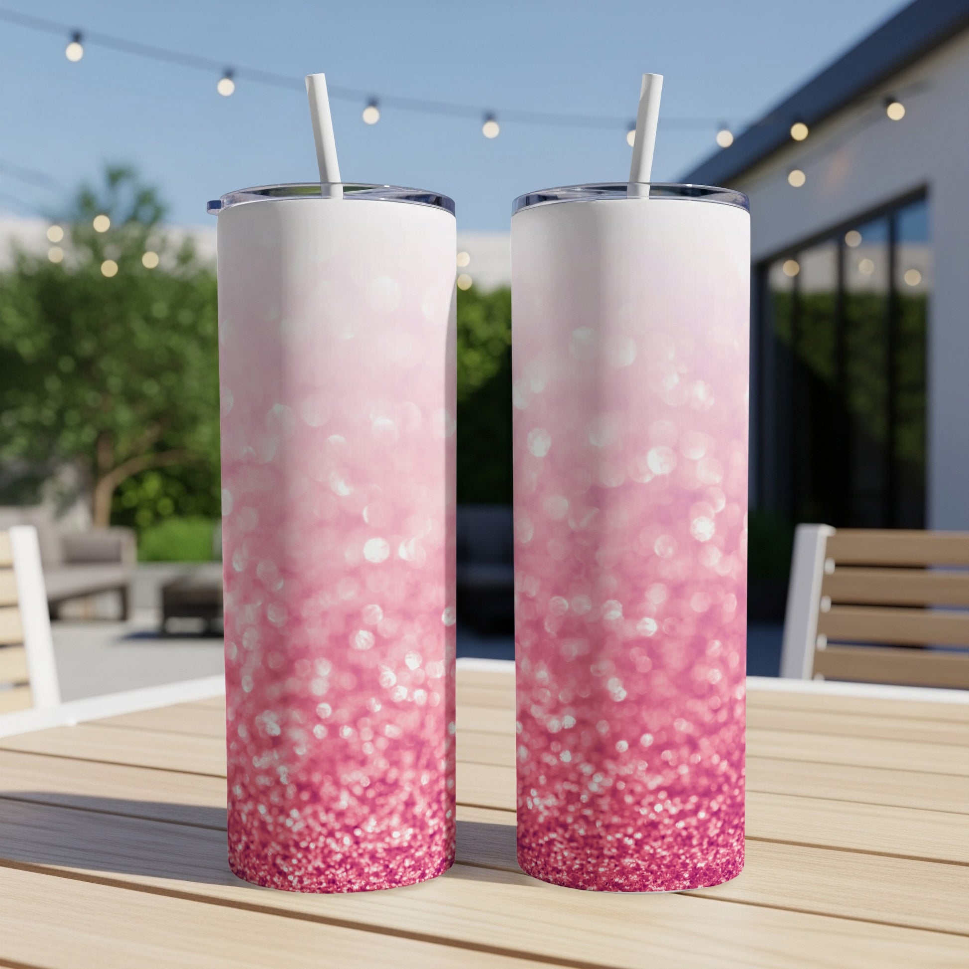 Two pink glitter tumblers with white straws on a wooden table.