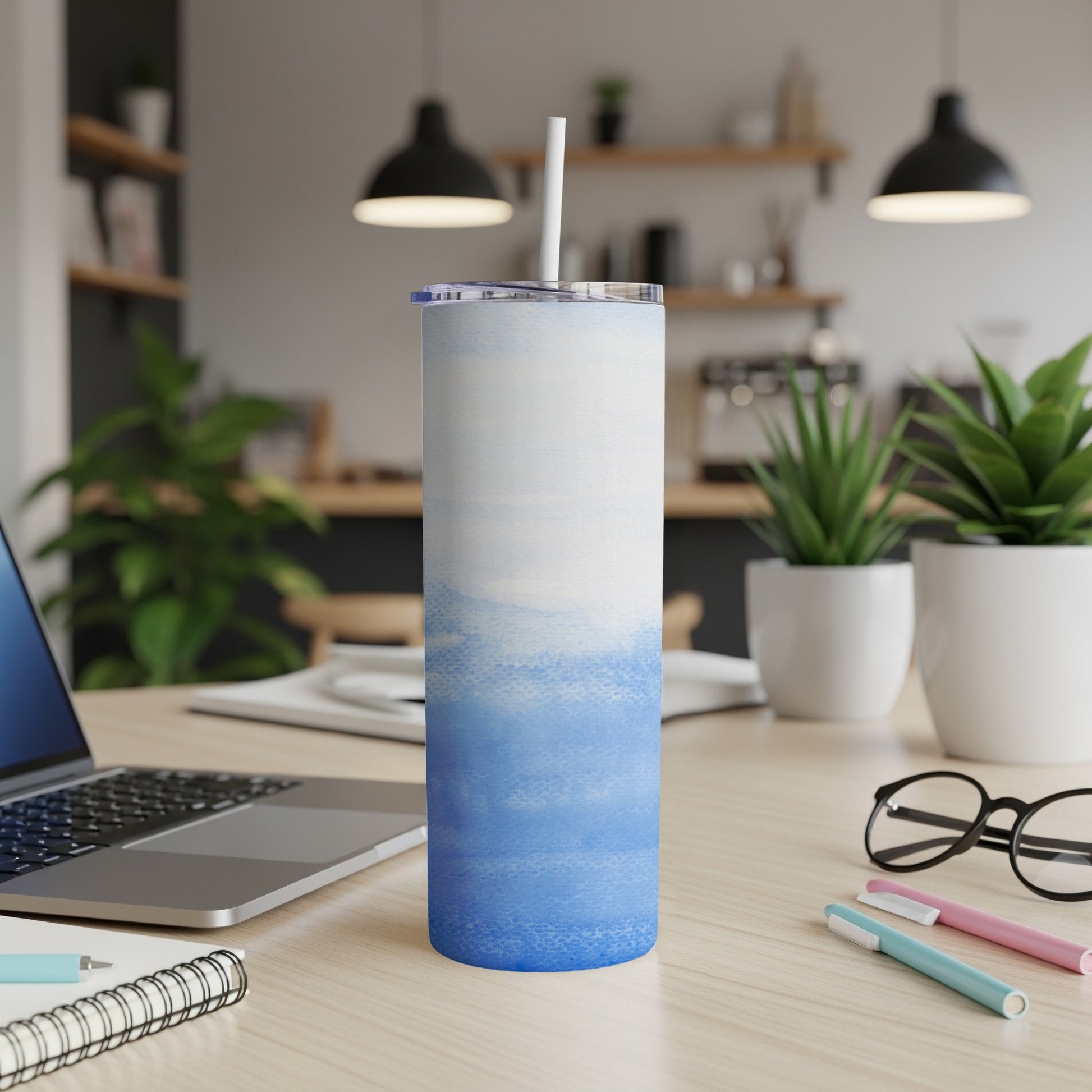 Blue and white abstract watercolor tumbler with straw on desk.