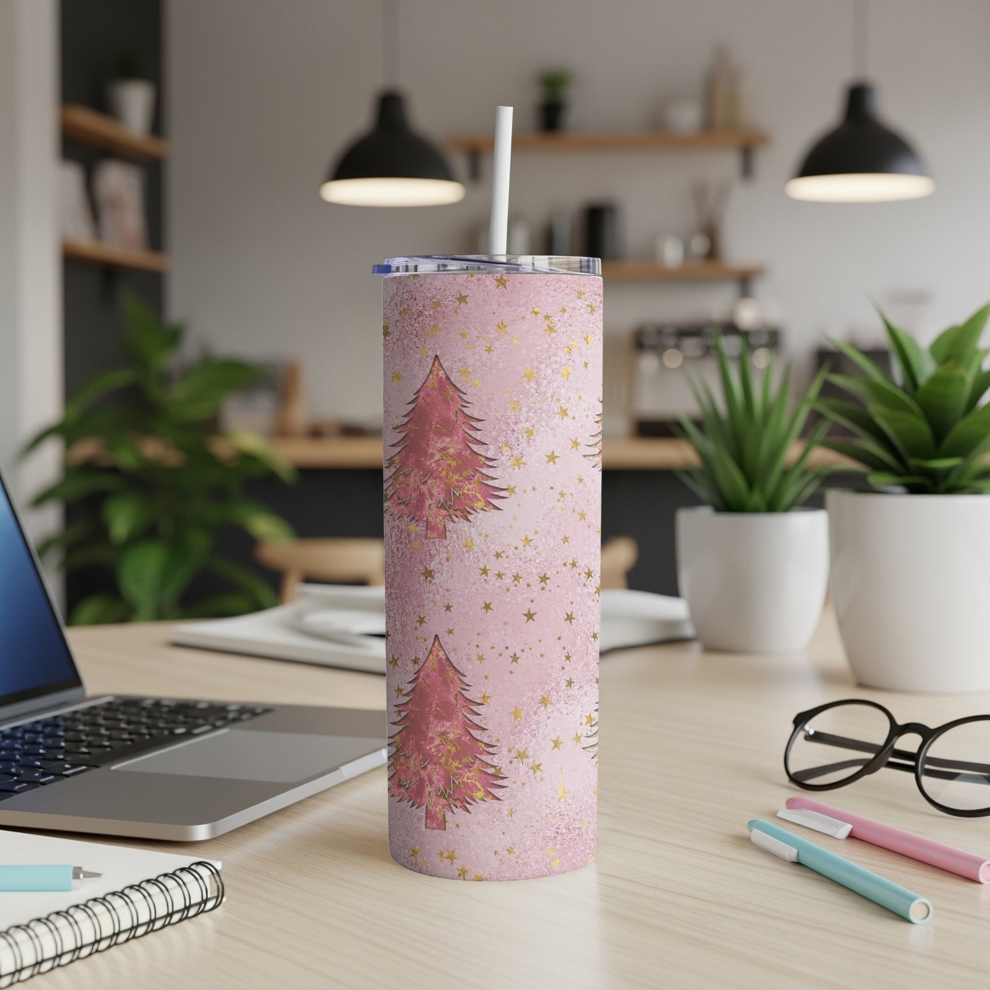 Pink tumbler with gold Christmas trees and stars, on a desk.