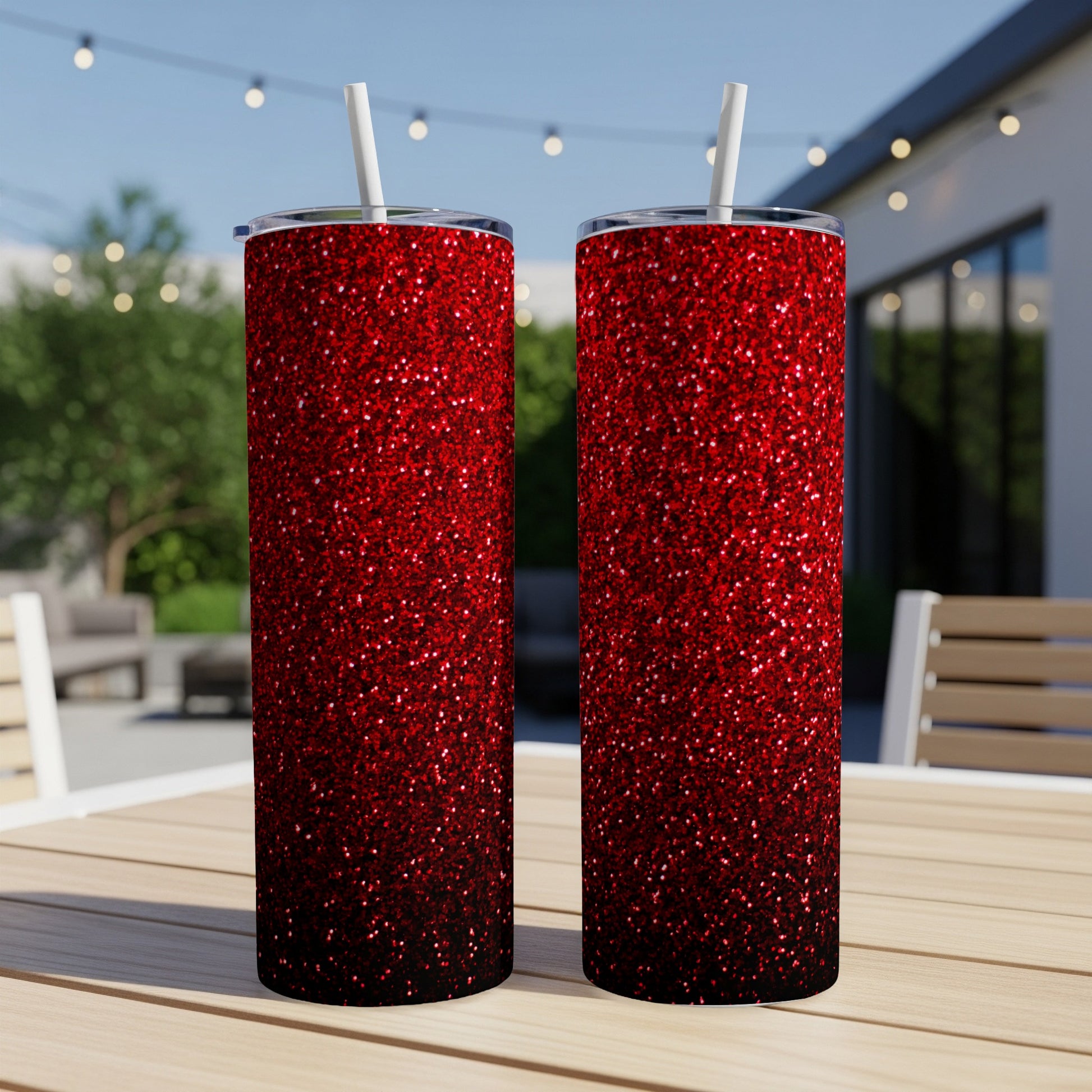 Two tall tumblers with a red glitter ombre design sit on a wooden table outdoors.