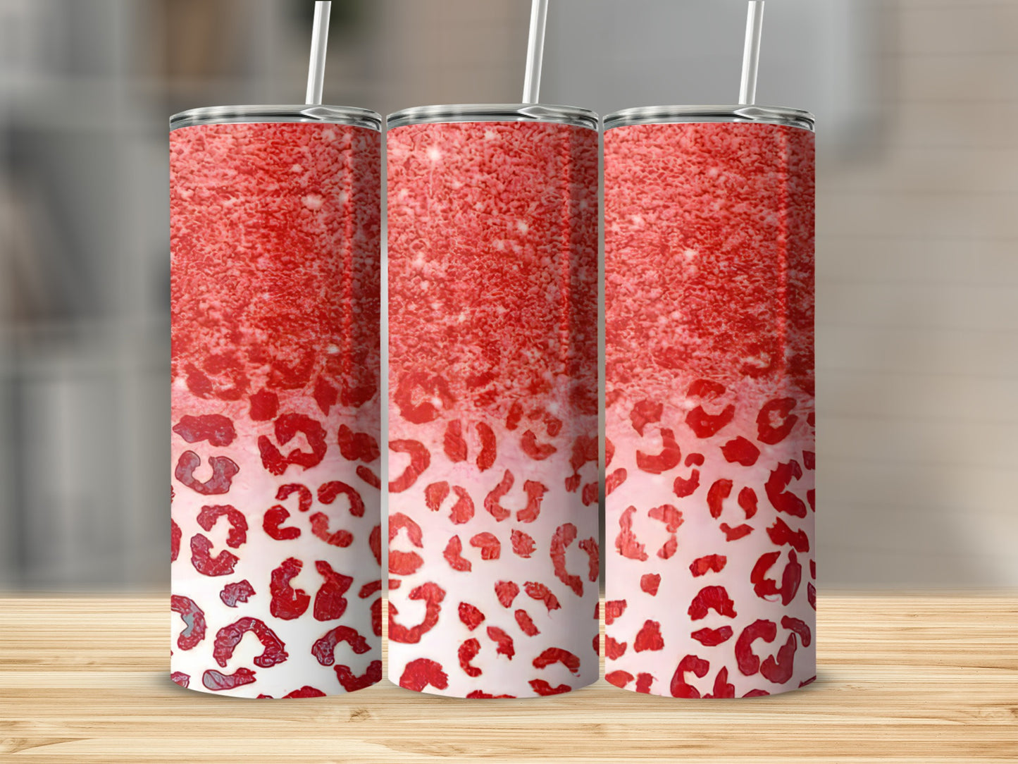 Three red glitter leopard print tumblers with straws on a wooden surface.
