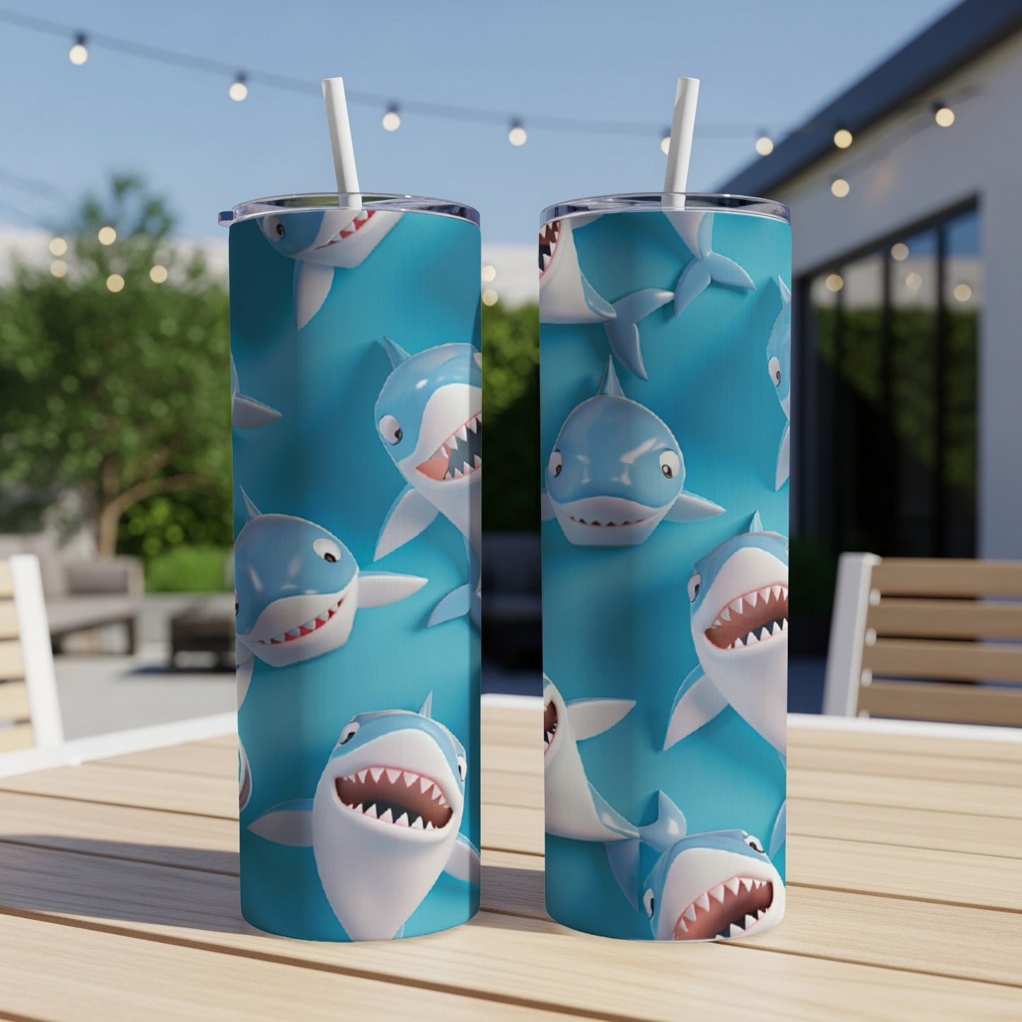 Two blue tumblers with repeating shark face pattern on outdoor table.