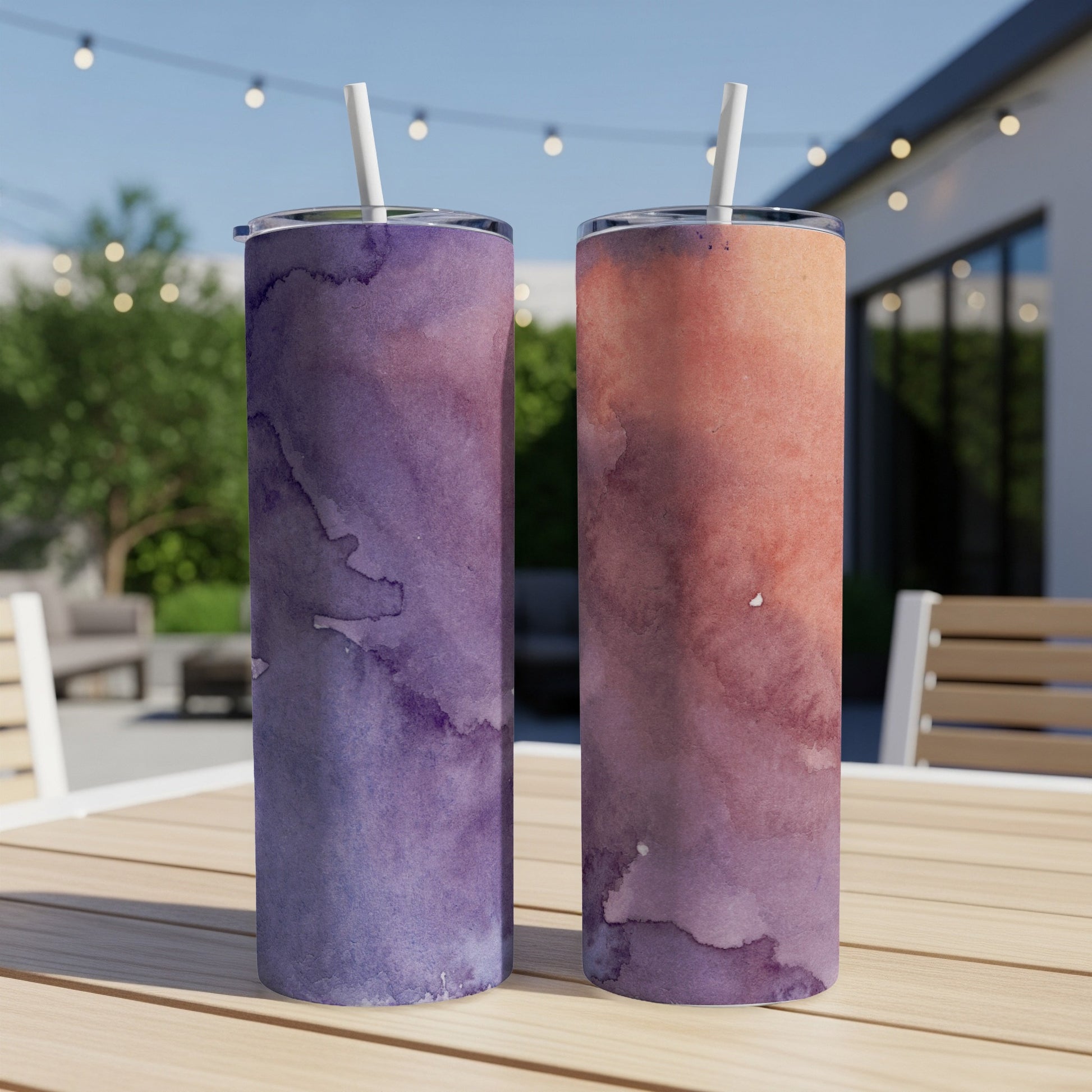 Two tumblers with purple and orange watercolor designs sit on a table.