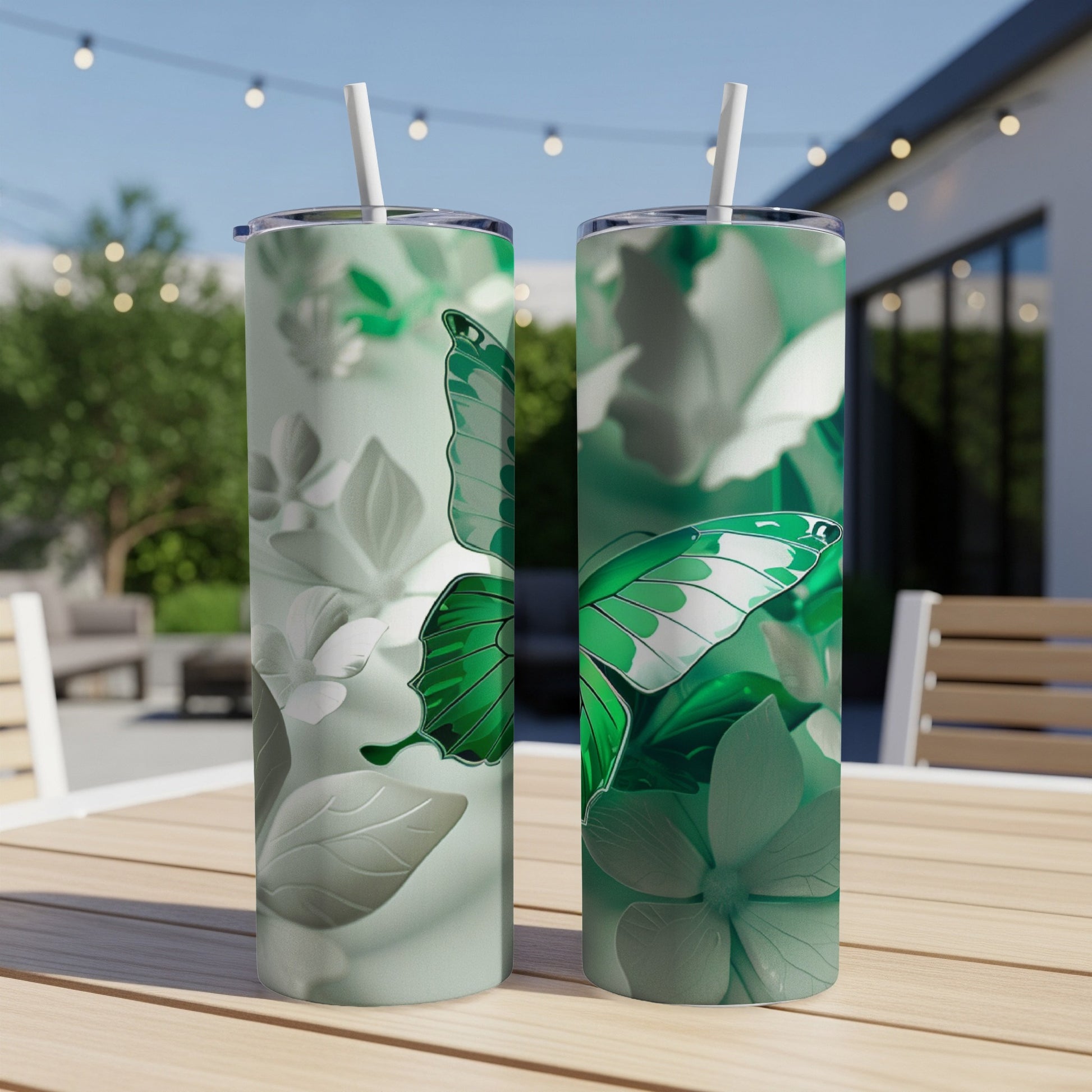 Two tall green tumblers with butterfly and floral designs sit on a table.