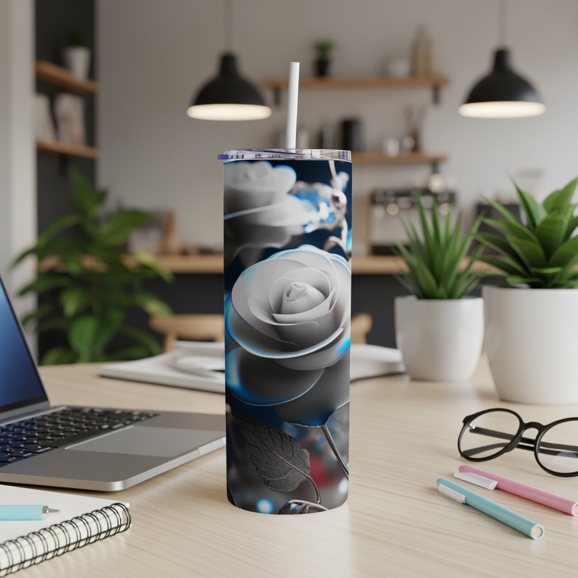Silver rose tumbler with white straw on a desk with laptop and pens.