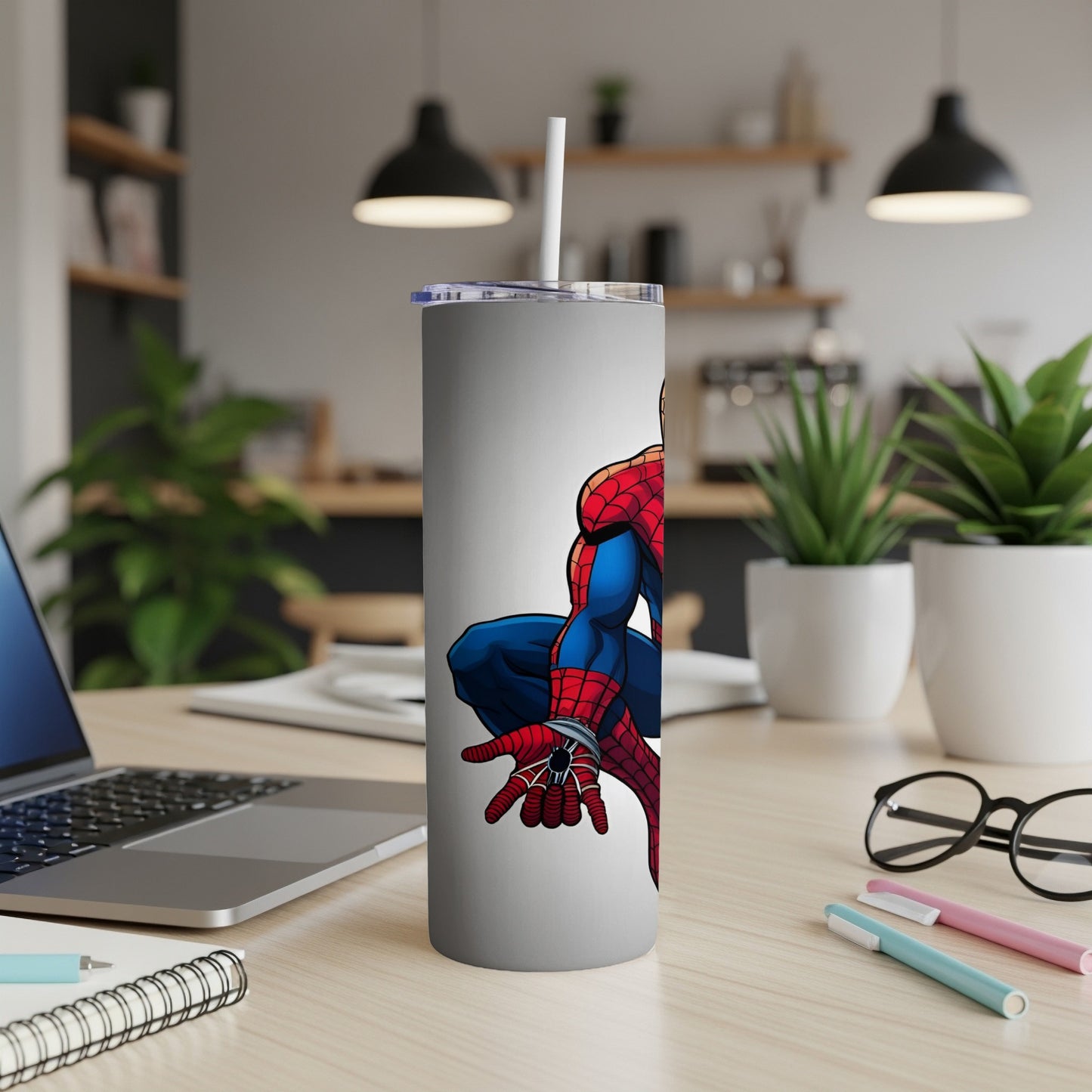 Spider-Man crouches on a white tumbler with a straw, desk background.