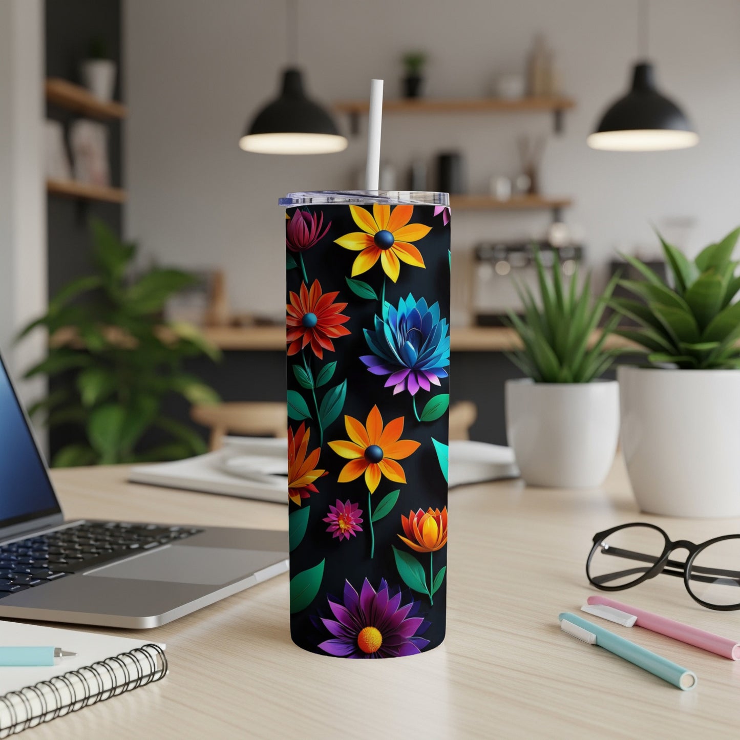 Black tumbler with colorful floral pattern, straw, on a desk.