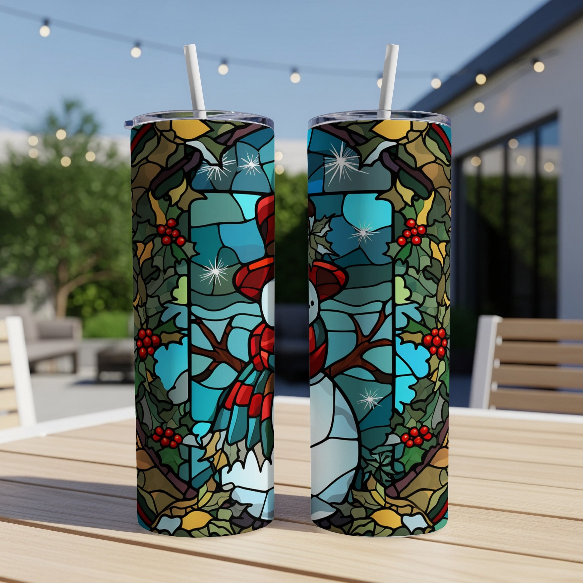 Two tumblers with stained glass snowman design on outdoor table.