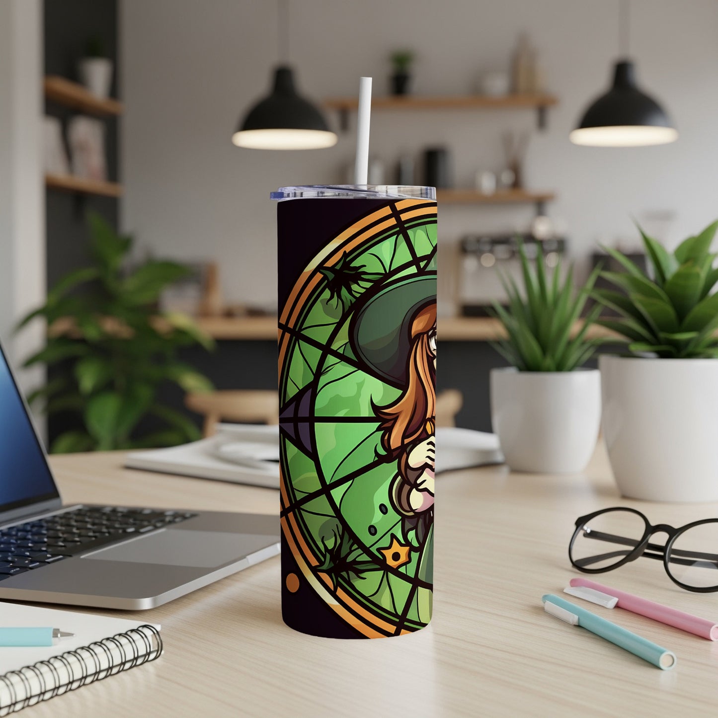 Witch illustration on a tall tumbler with a straw, on a desk.