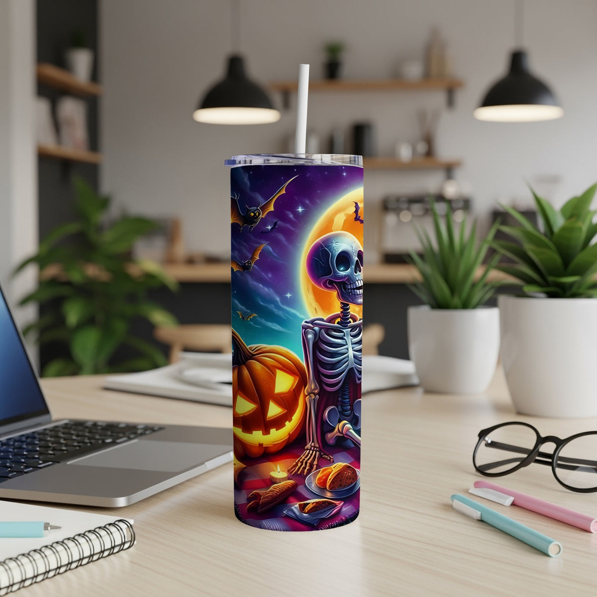 Halloween tumbler with skeleton, pumpkin, bats, and moon on a desk.