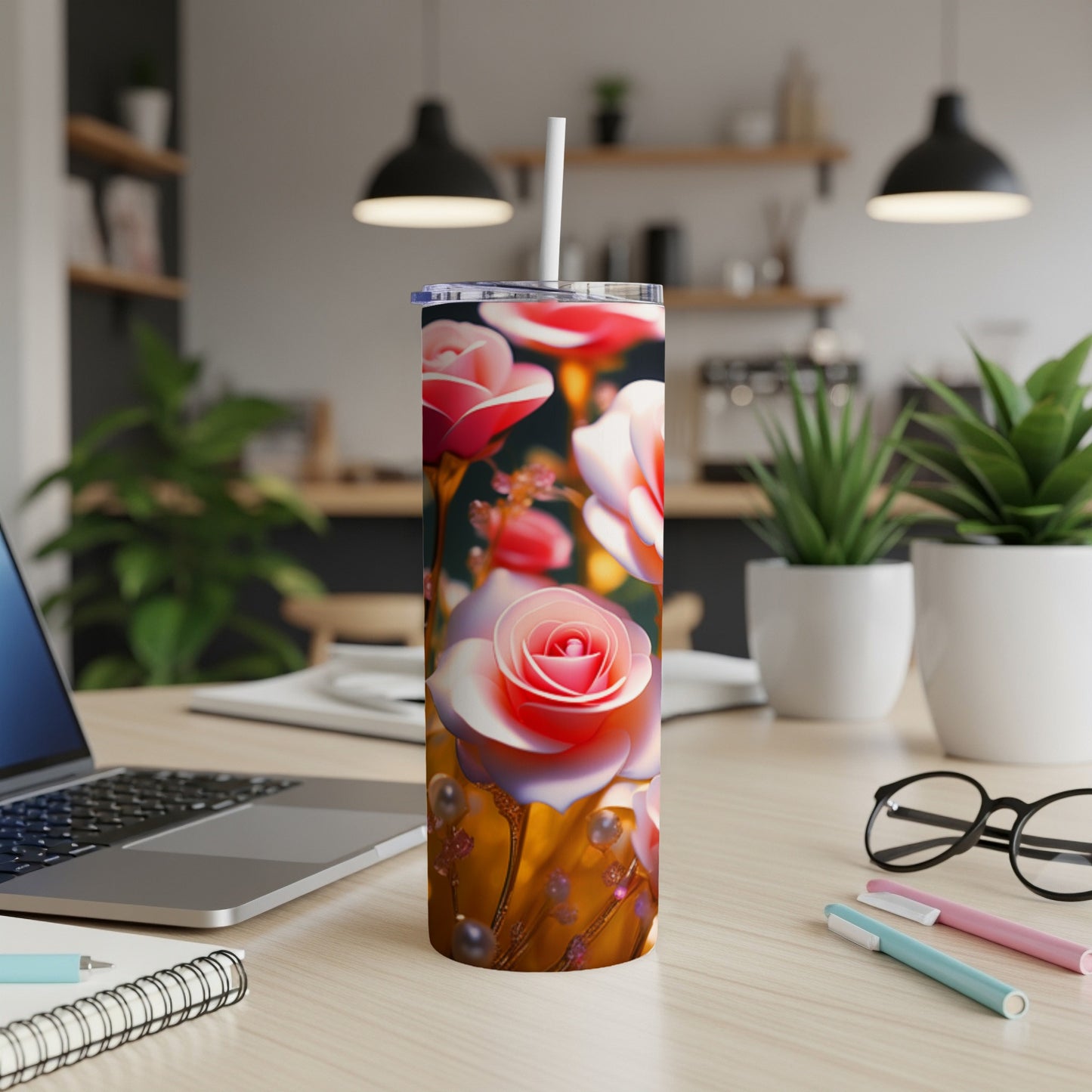 Pink roses on a tumbler with a white straw, laptop, and pens on a desk.