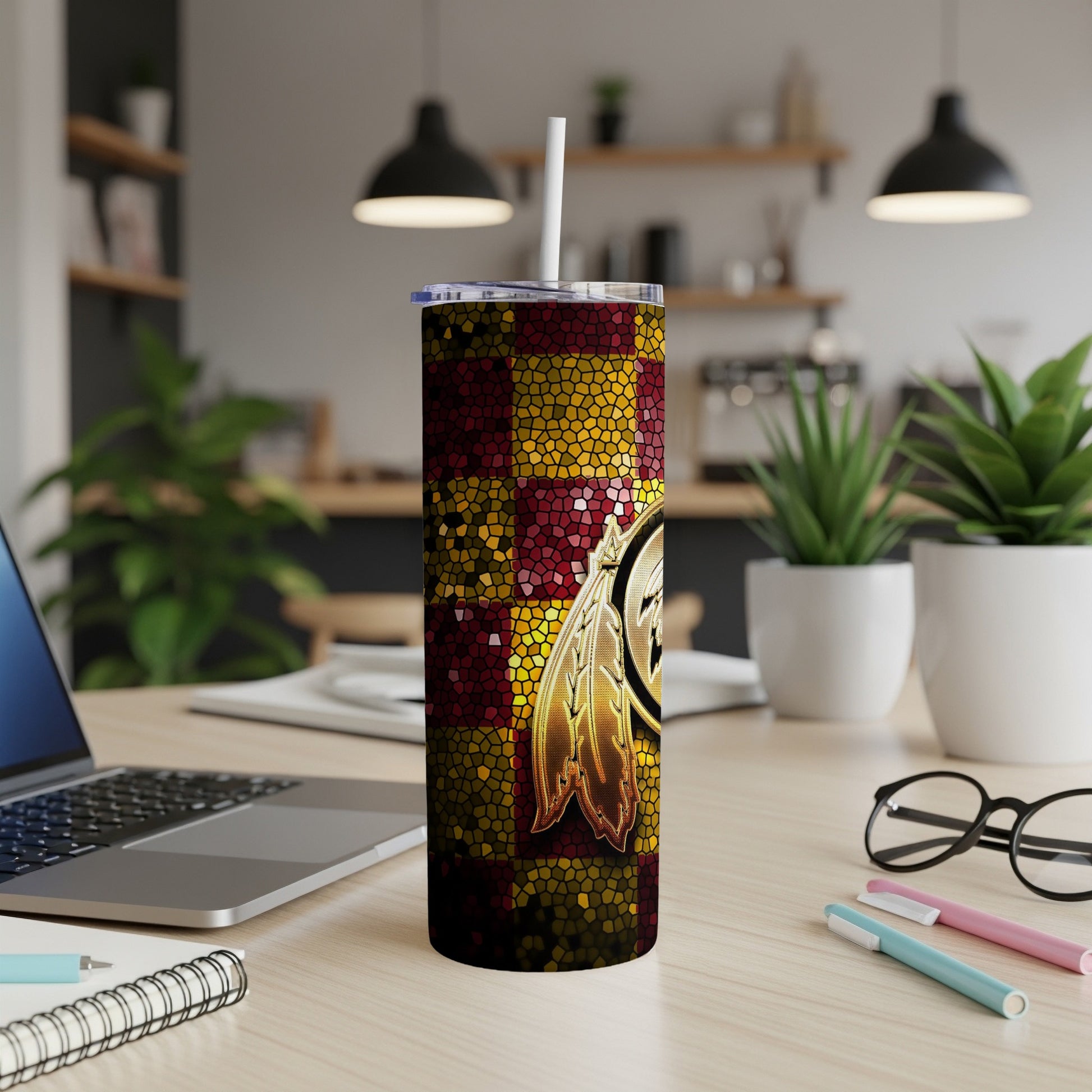 Tumbler with Washington Redskins logo and mosaic pattern, near laptop and plants.