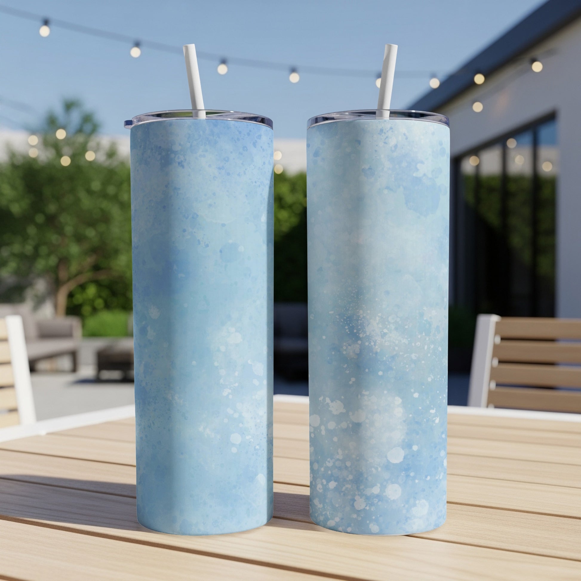 Two blue watercolor tumblers with white specks and straws on a table.