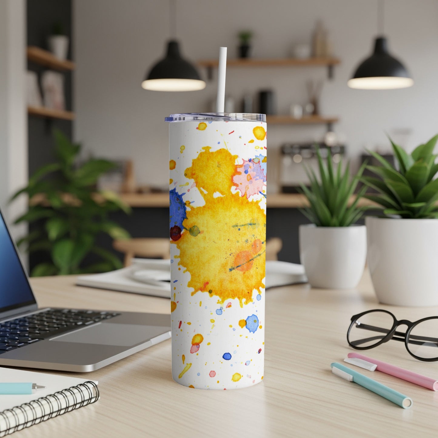 White tumbler with colorful abstract paint splatters and a straw.