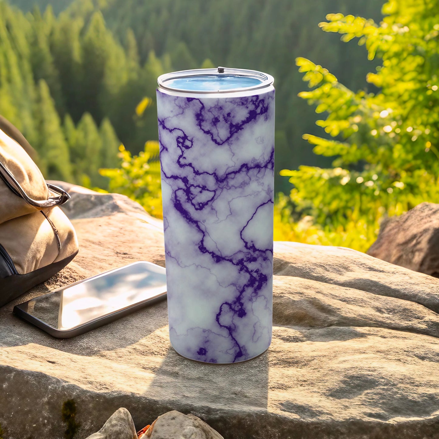 Purple marble patterned tumbler on rock with phone and backpack.