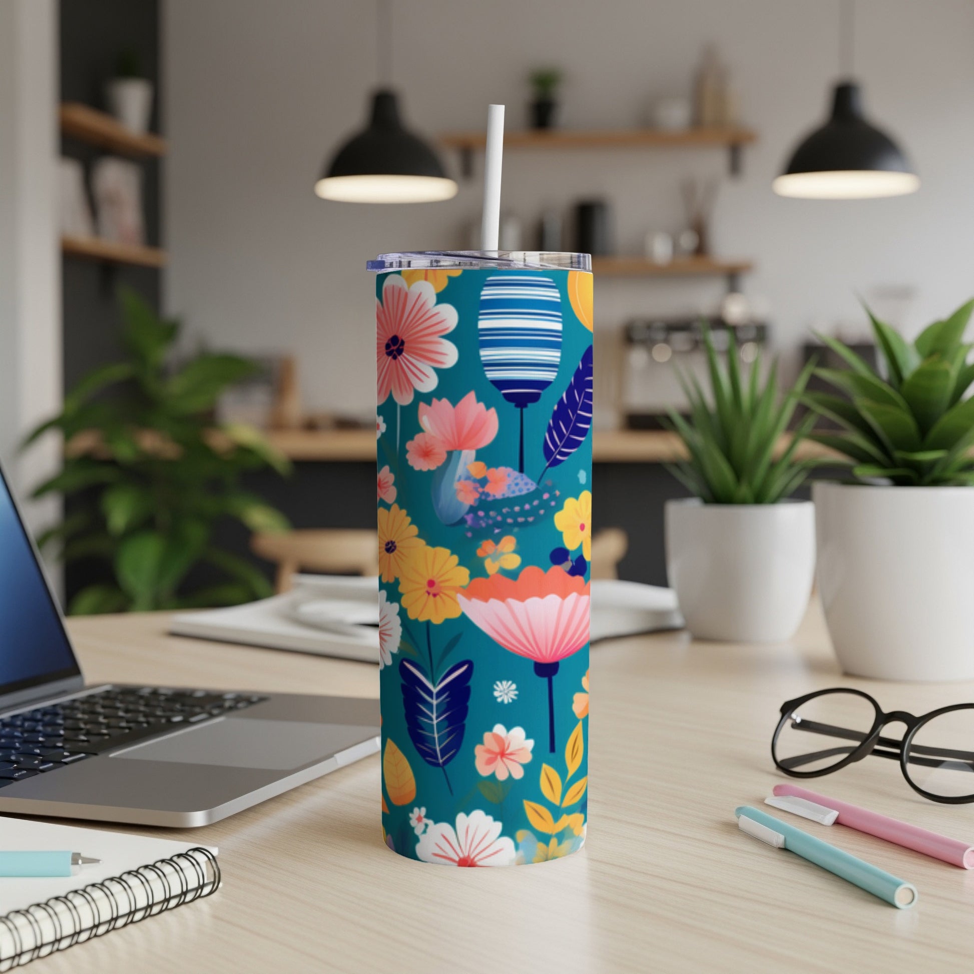 Teal tumbler with colorful floral and striped patterns, straw, and laptop.