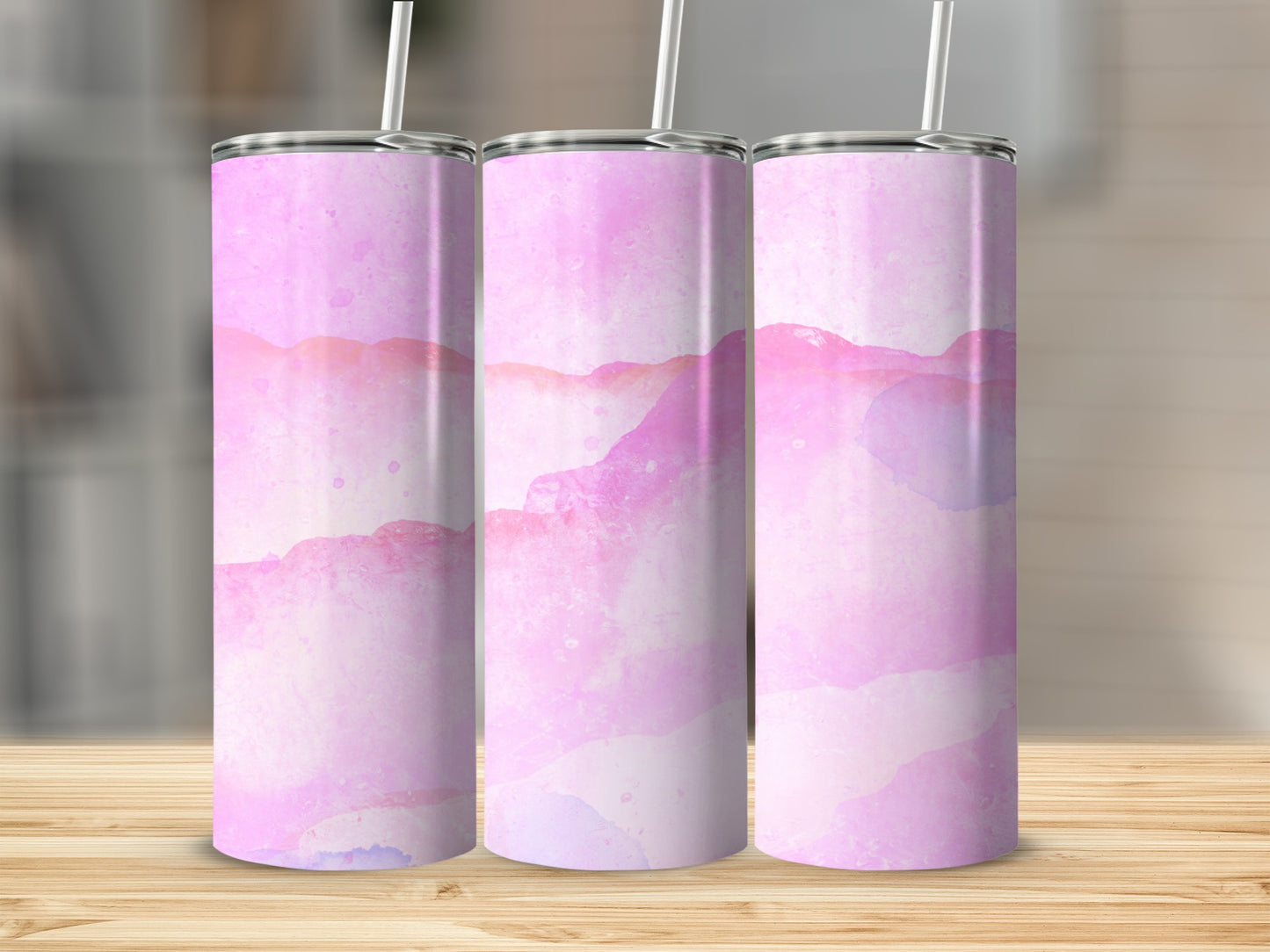 Three pink watercolor tumblers with straws on a wooden surface.