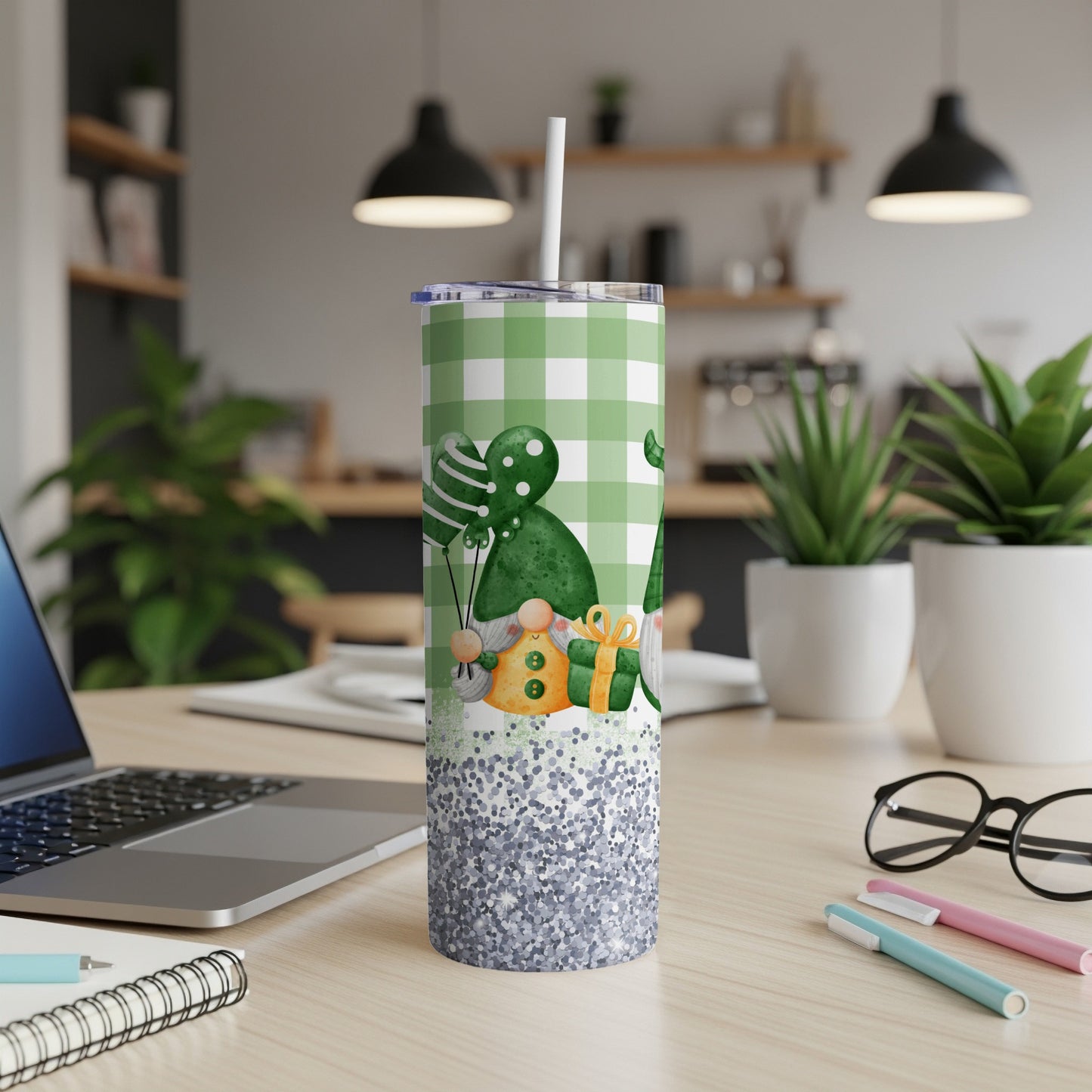 Green plaid tumbler with gnomes, balloons, and glitter on a desk.