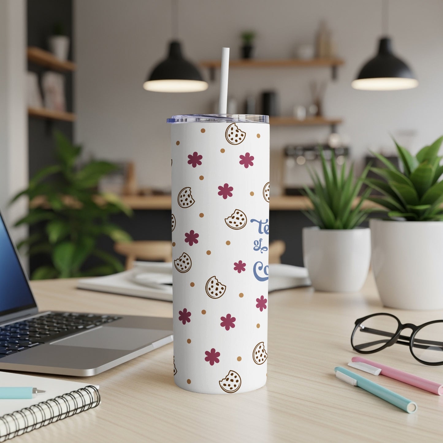 White tumbler with cookie and flower pattern, straw, on desk.