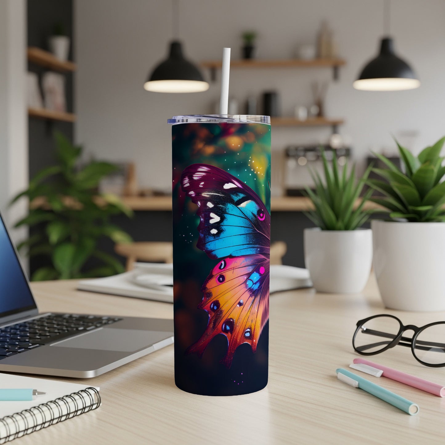 Tumbler with a colorful butterfly design on a desk with a laptop and pens.