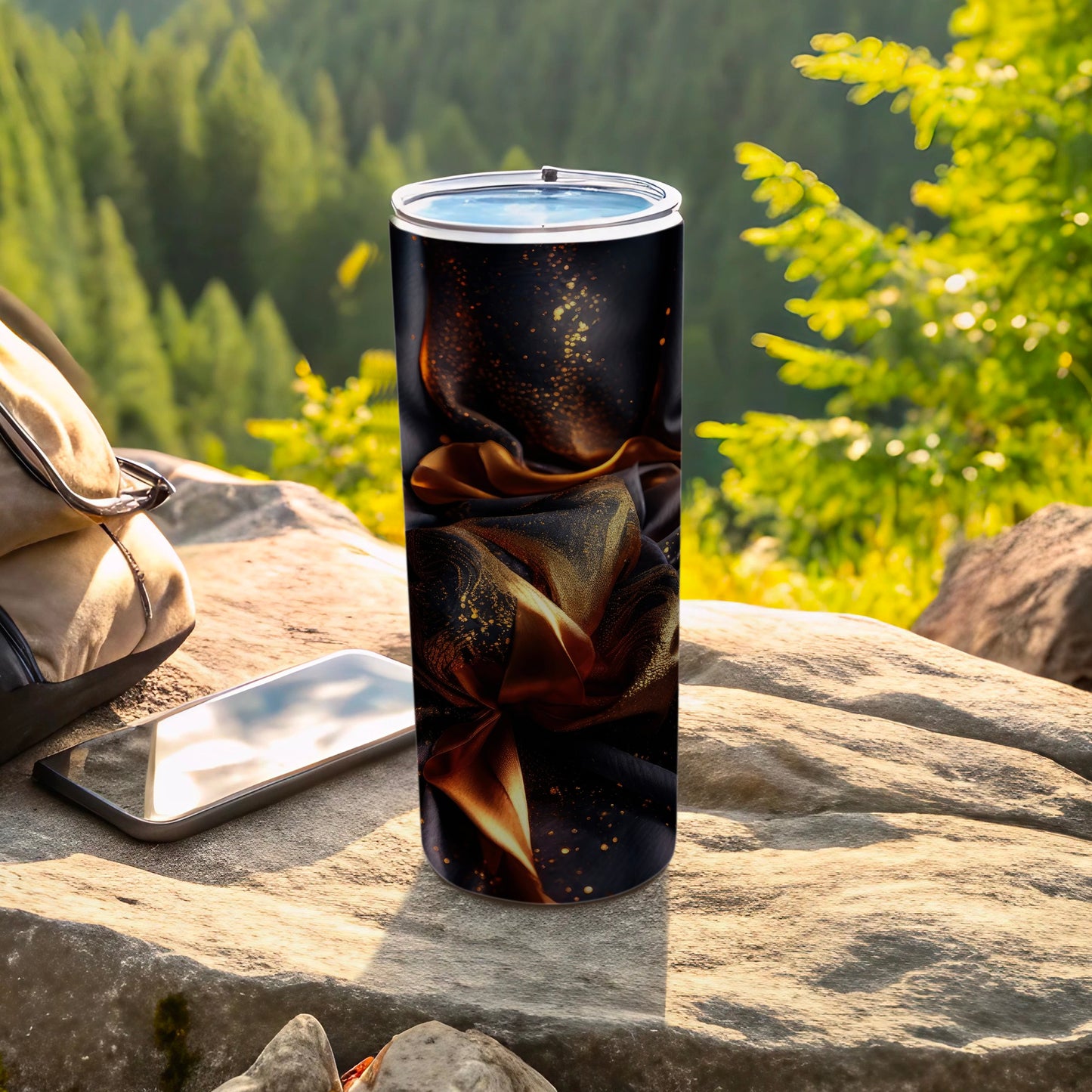 Black tumbler with gold glitter and swirling fabric design on rocks.
