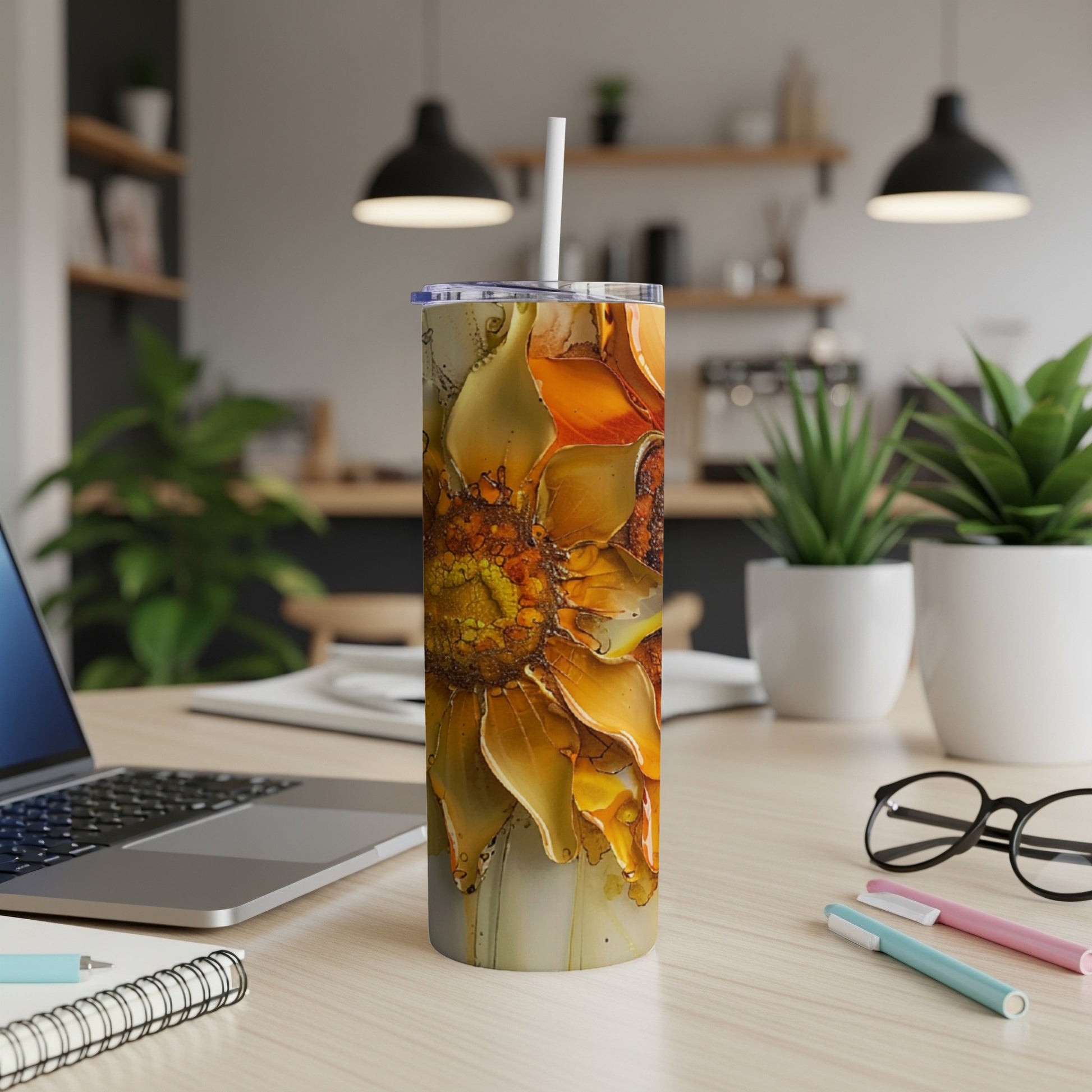 Sunflower tumbler with straw on desk with laptop and pens.