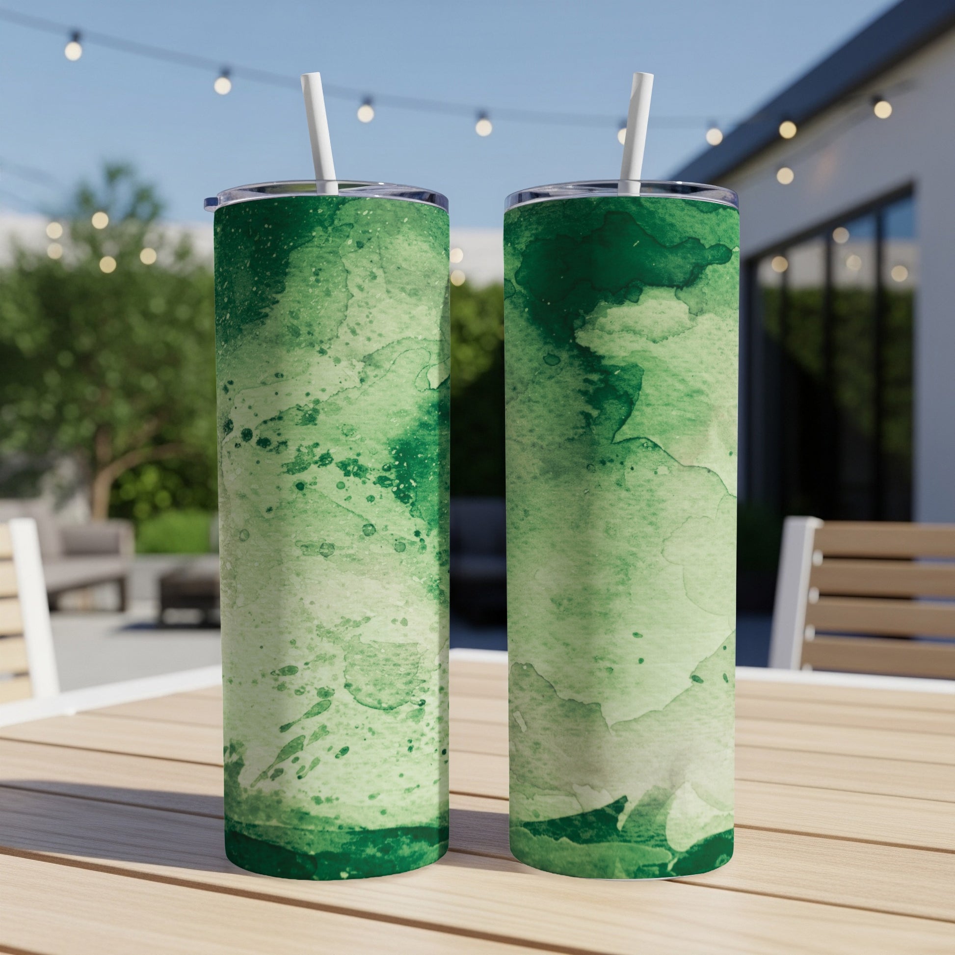 Two green watercolor print tumblers with straws on a wooden table.