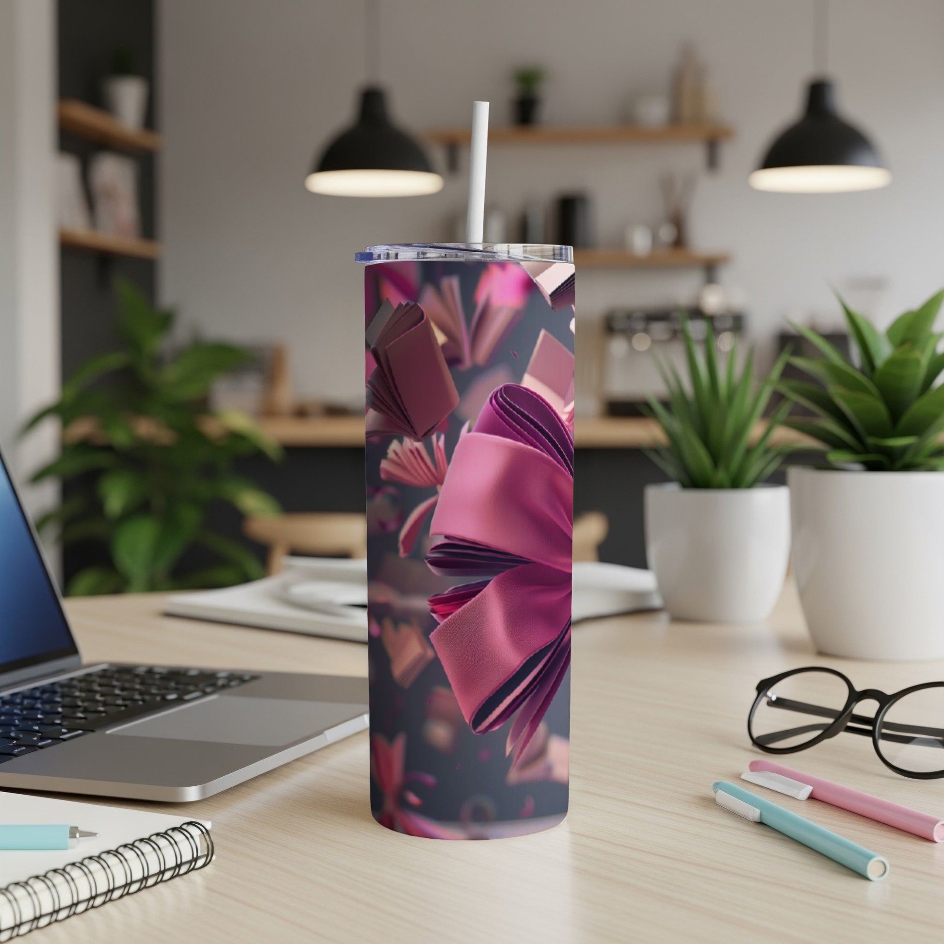 Pink ribbon and floating books on a wooden desk with a laptop and pens.