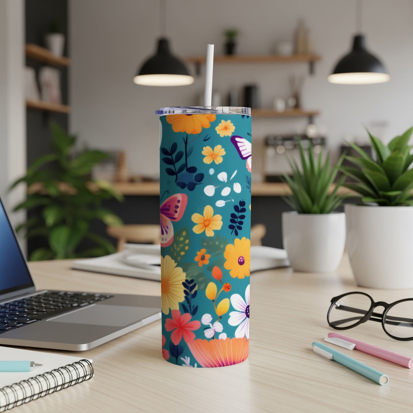 Teal tumbler with colorful floral and butterfly pattern on a desk.