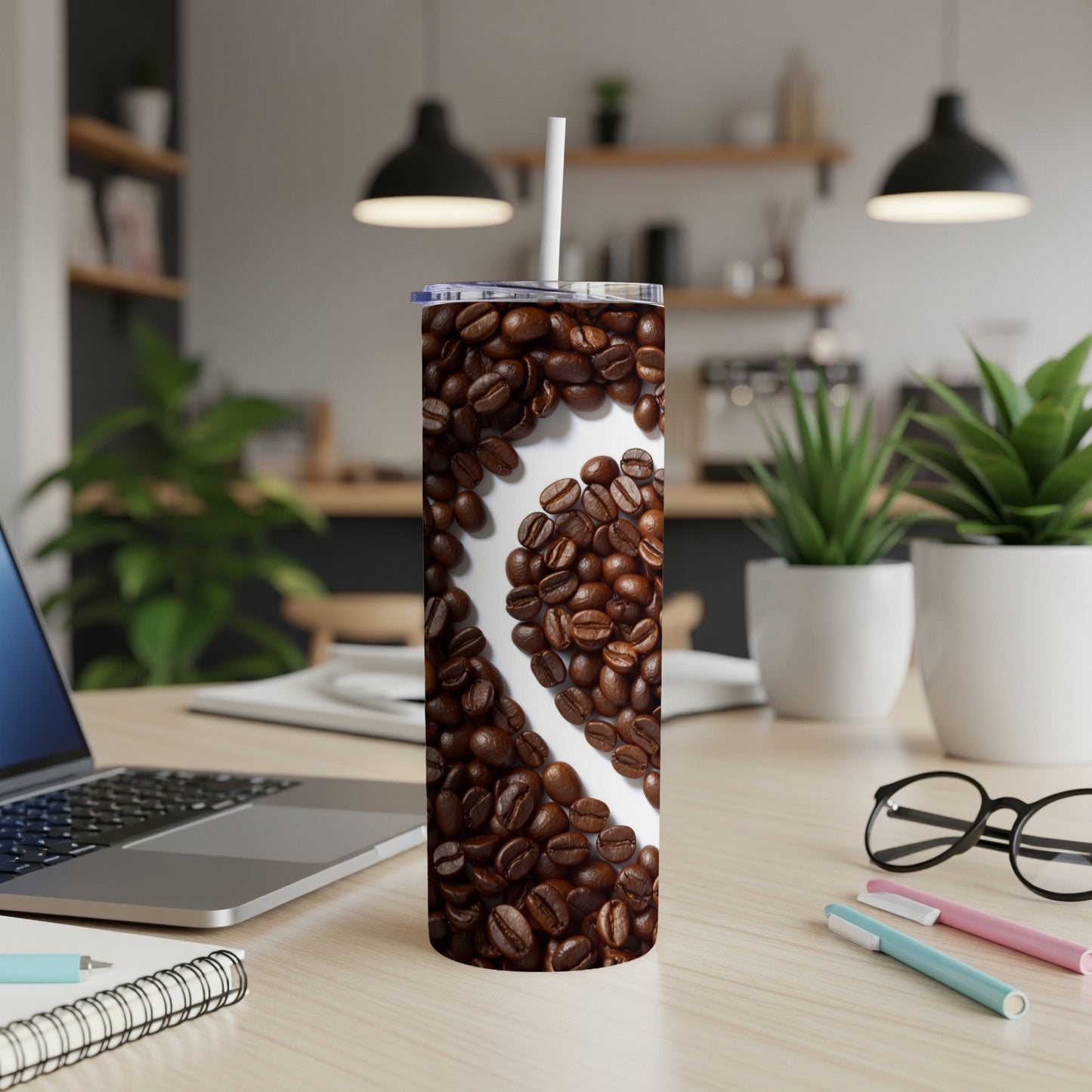 Tumbler with heart-shaped coffee bean pattern on desk with laptop.
