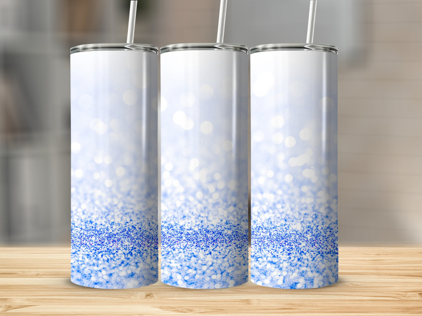 Three white tumblers with blue glitter design on a wooden surface.