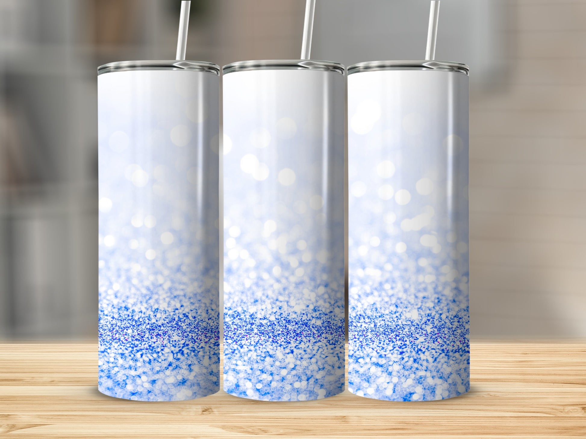 Three white tumblers with blue glitter design on a wooden surface.