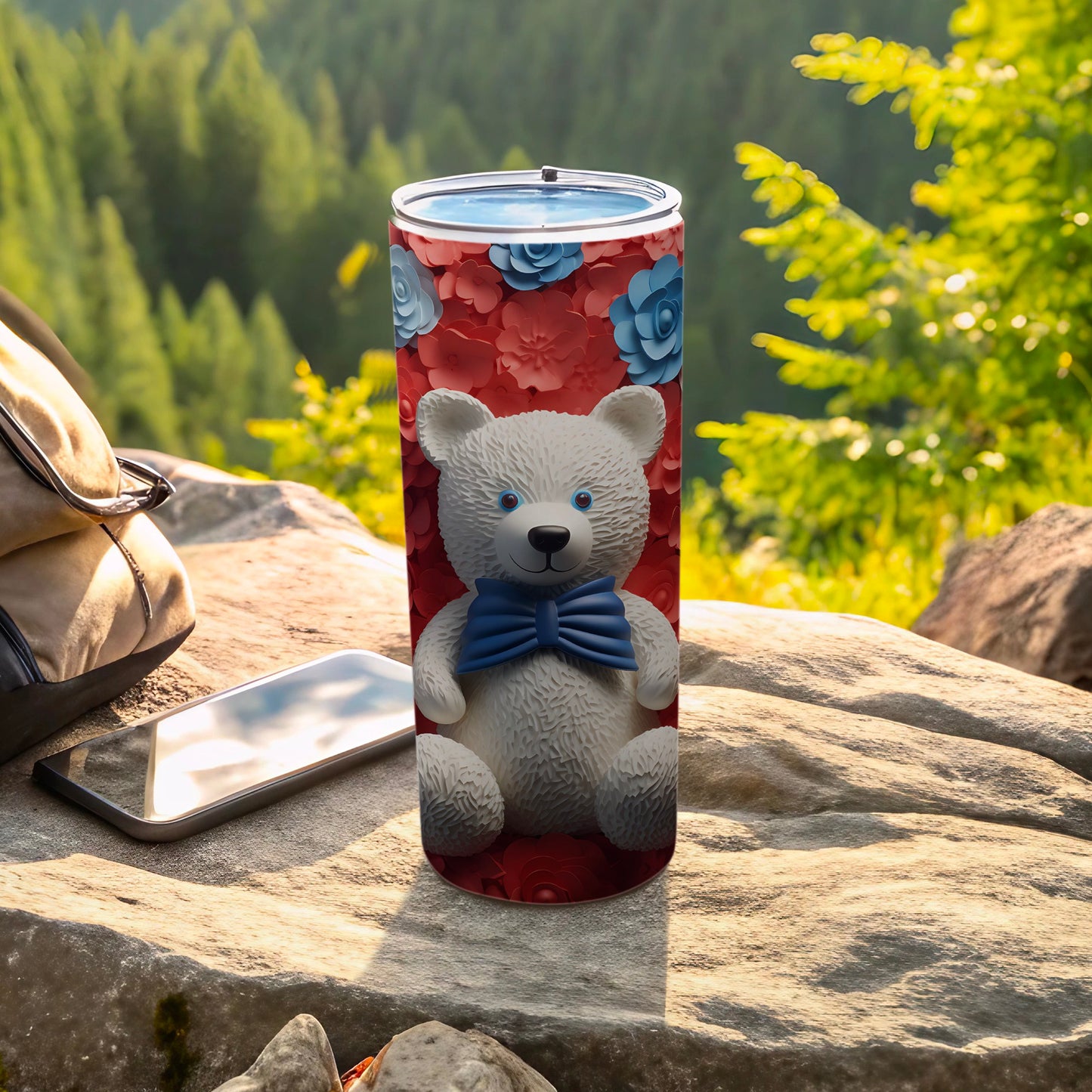 White teddy bear with blue bow on a floral tumbler, outdoors.