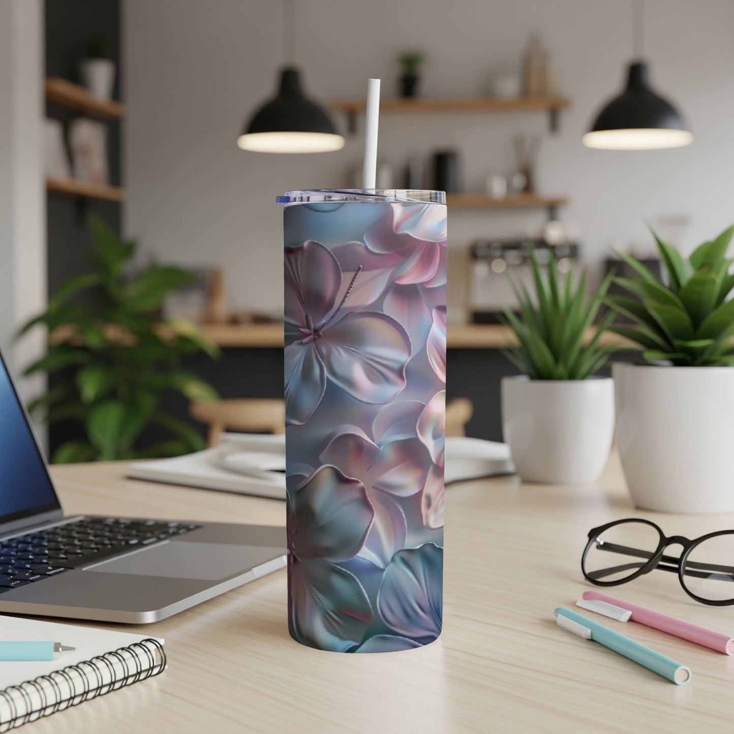 Floral tumbler with straw on a desk next to a laptop and pens.