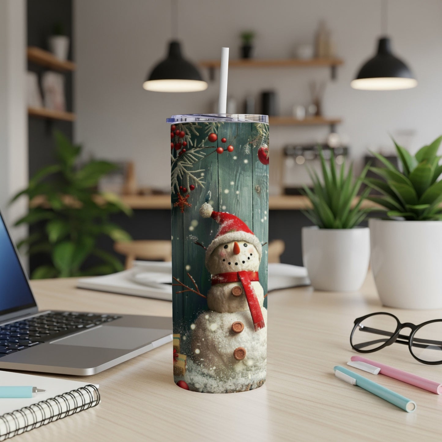 Snowman tumbler with red scarf and Santa hat on a wooden desk.