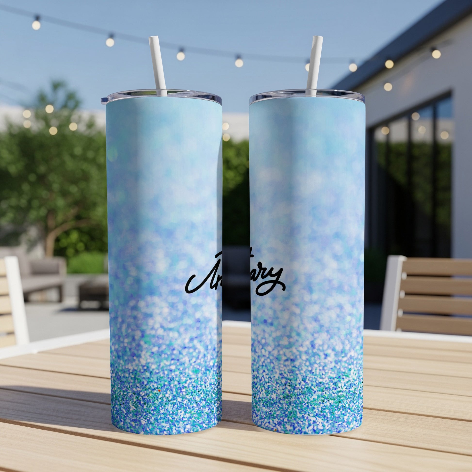 Two glittery blue tumblers with straws on an outdoor table.